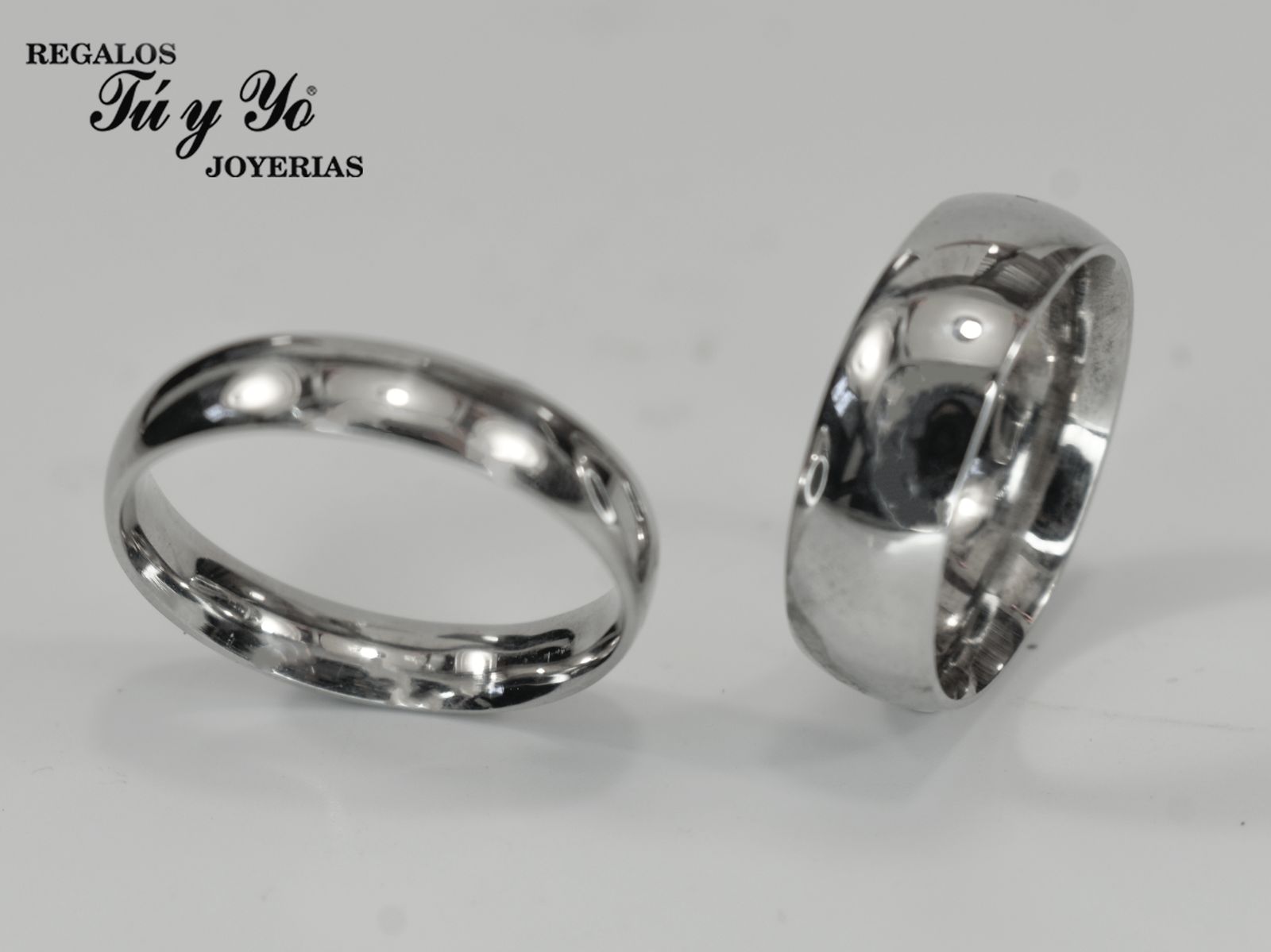 Two silver rings on a reflective surface, with a 'Regalos Tú y Yo Joyerías' logo in the top left corner.