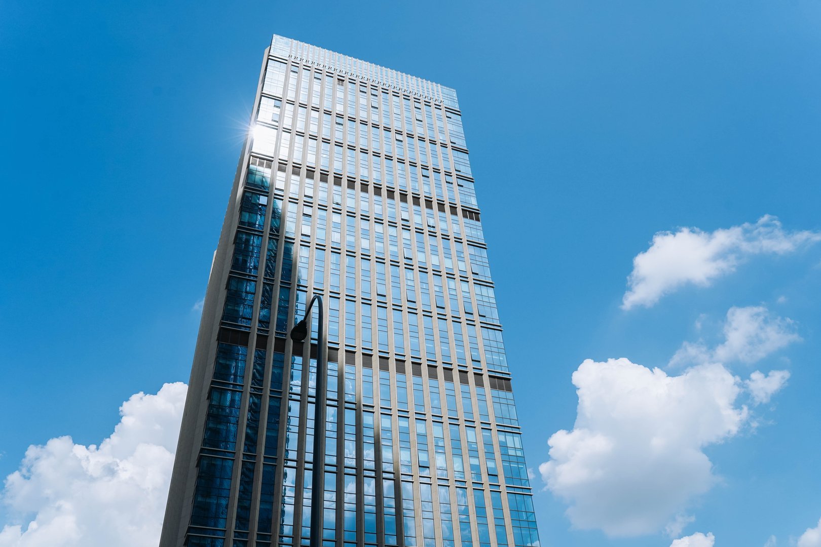 A modern glass office building reflecting the blue sky and white clouds, creating a sleek and contemporary urban aesthetic.