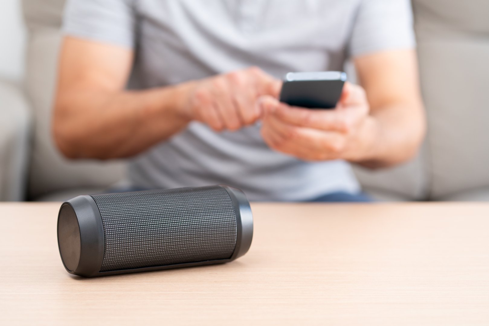 Man enjoys his favorite tunes while scrolling through his smartphone.Speaker on the table for relaxation and entertainment.Technologies in AI artificial intelligence systems