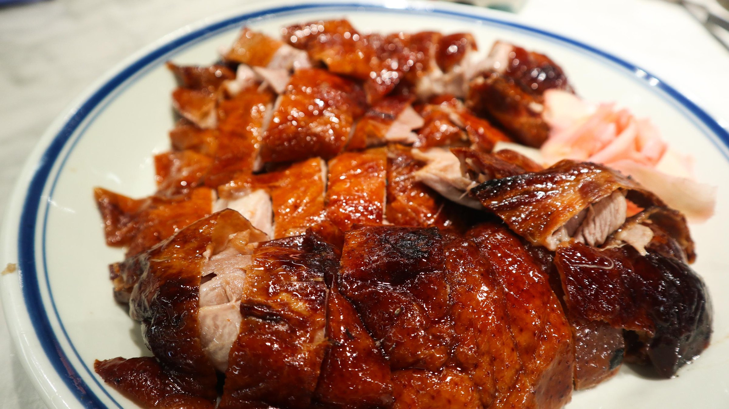 close up of Cantonese roasted goose cut into pieces with ginger slices on the side