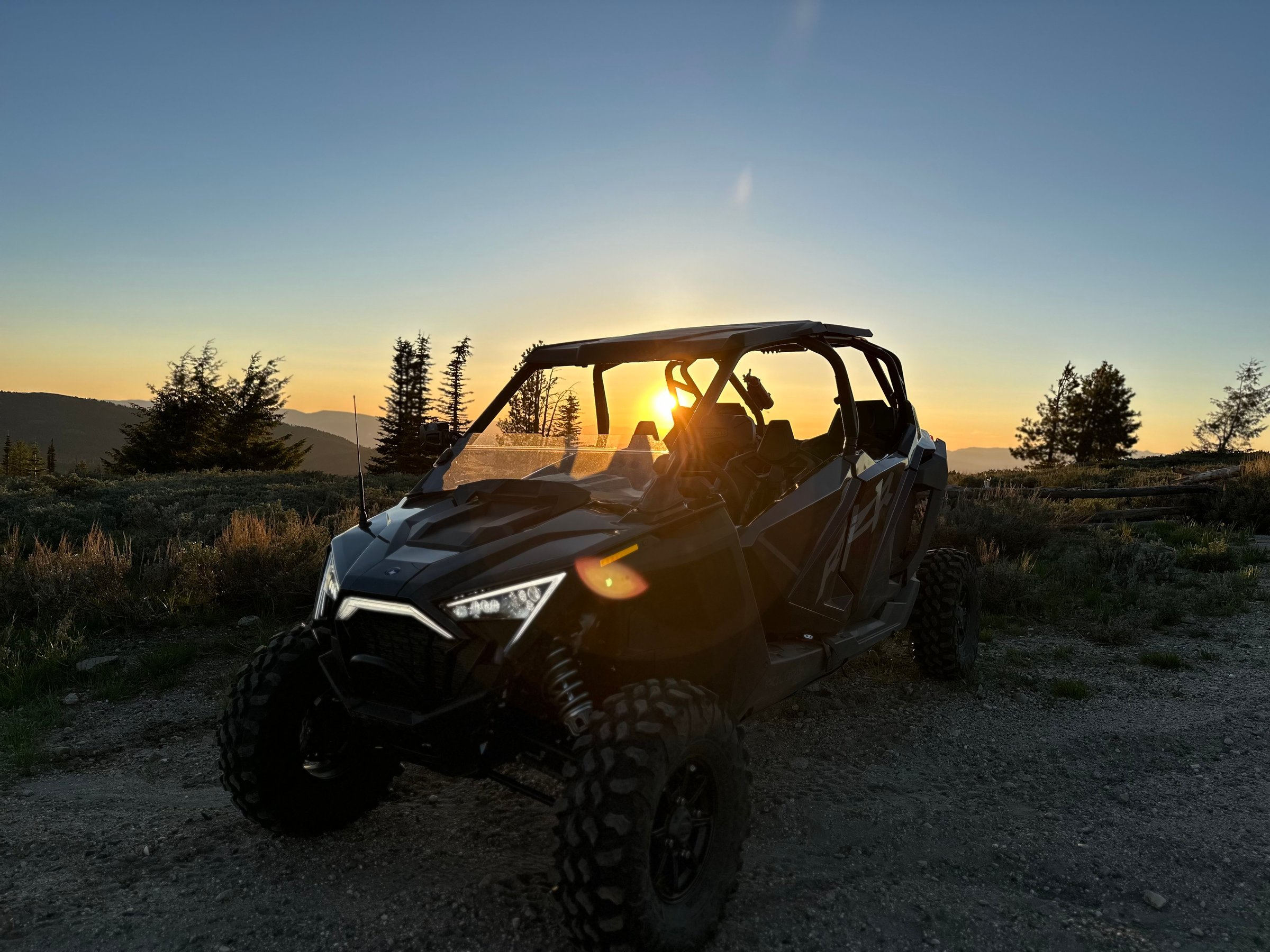 Off-road vehicle on a dirt trail at sunset with trees and mountains in the background.
