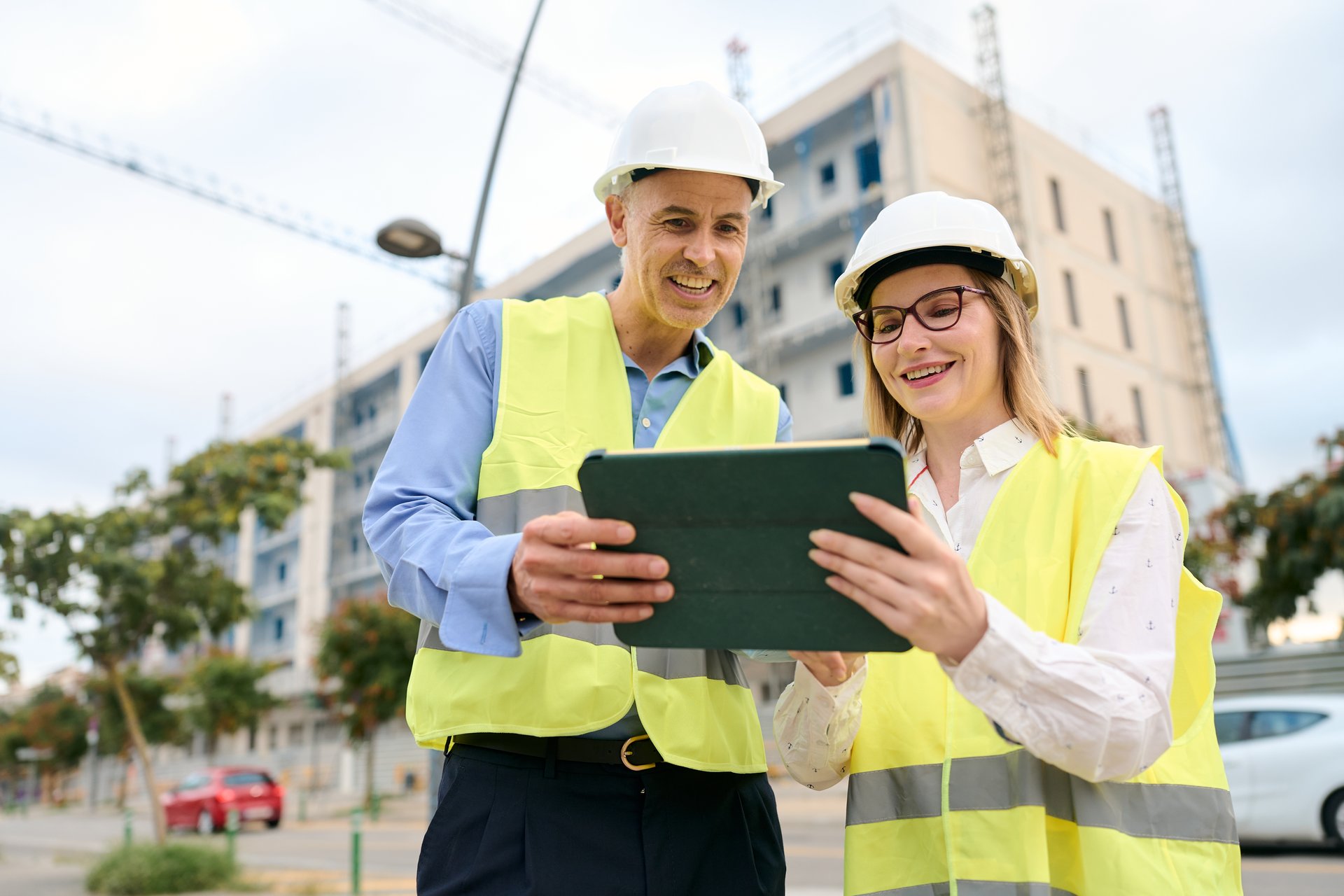 Construction engineers wearing safety vests and hard hats discussing building plans on a tablet at a construction site