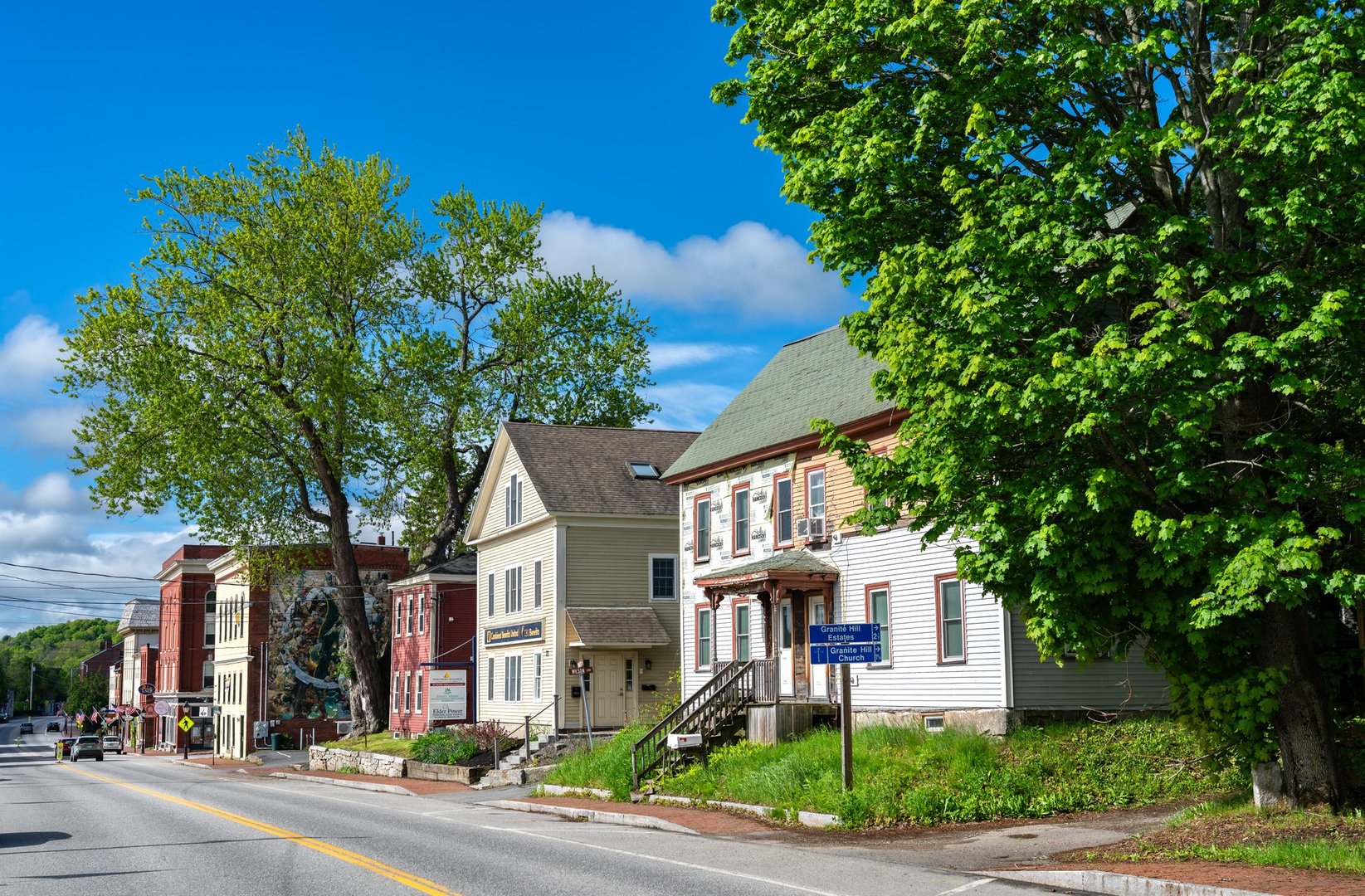 Hallowell, Maine - May 25, 2025: Colorful 19th-century buildings line Water Street in the small riverfront town of Hallowell, United States. A mural, leafy trees, and vintage signage contribute to the charm of this historic New England downtown.