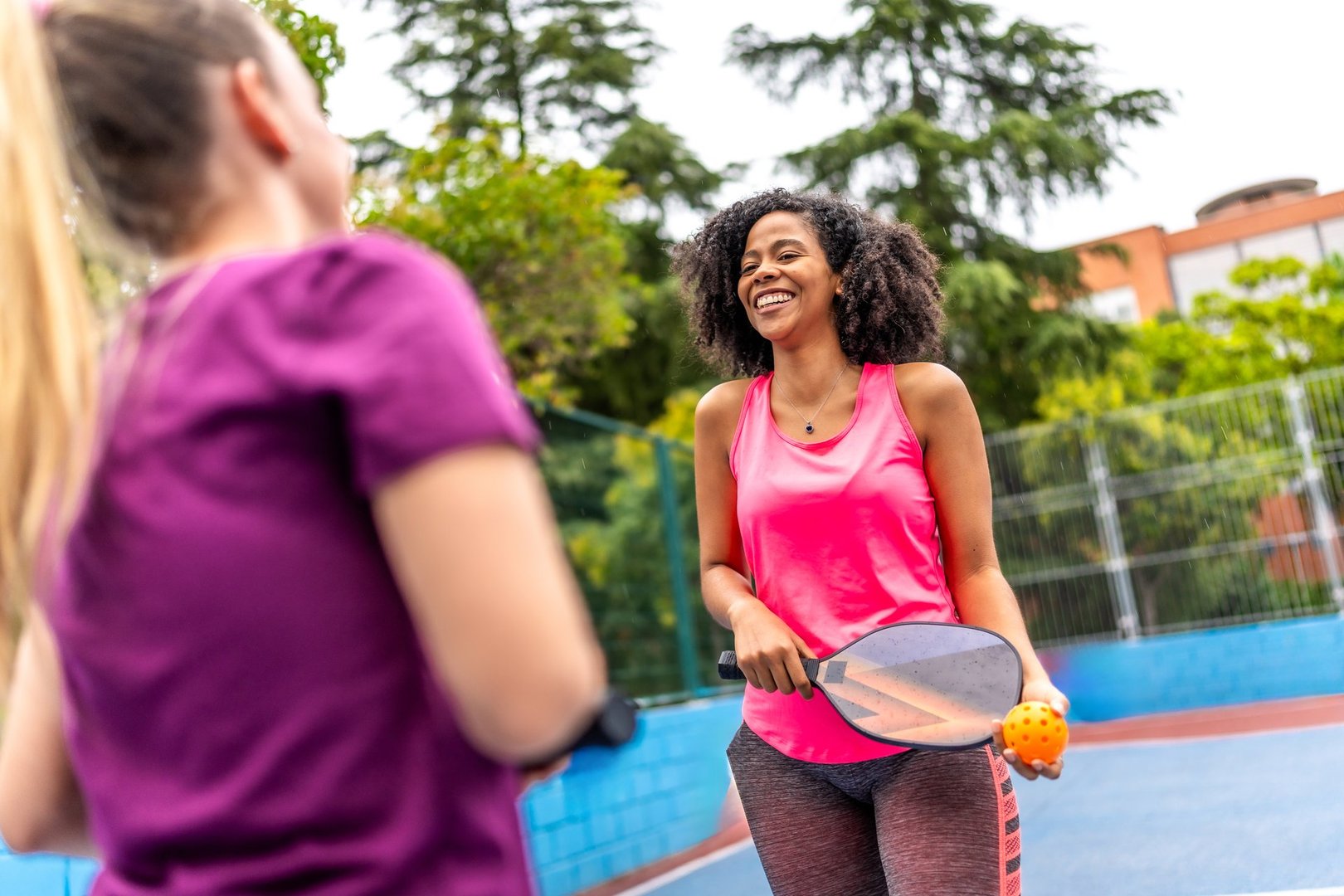 Happy pair of multi-ethnic women playing pickelball in an outdoor court