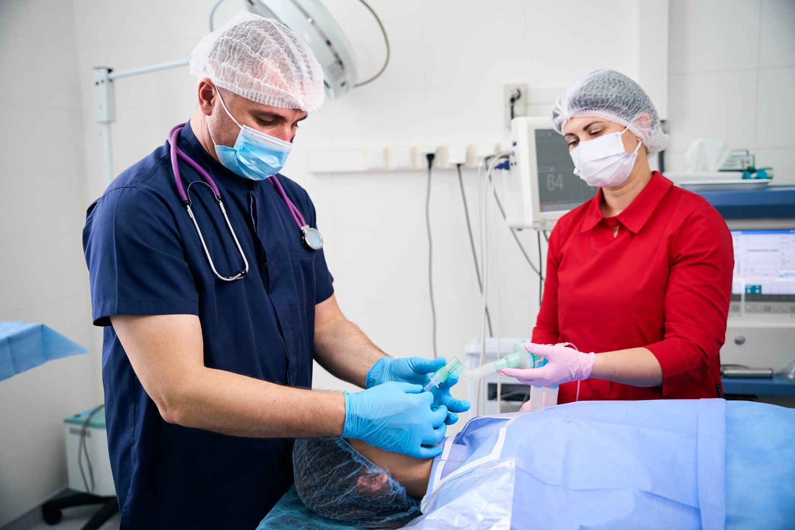 Anesthesiologist works in an operating room with an assistant, a patient lies on the operating table