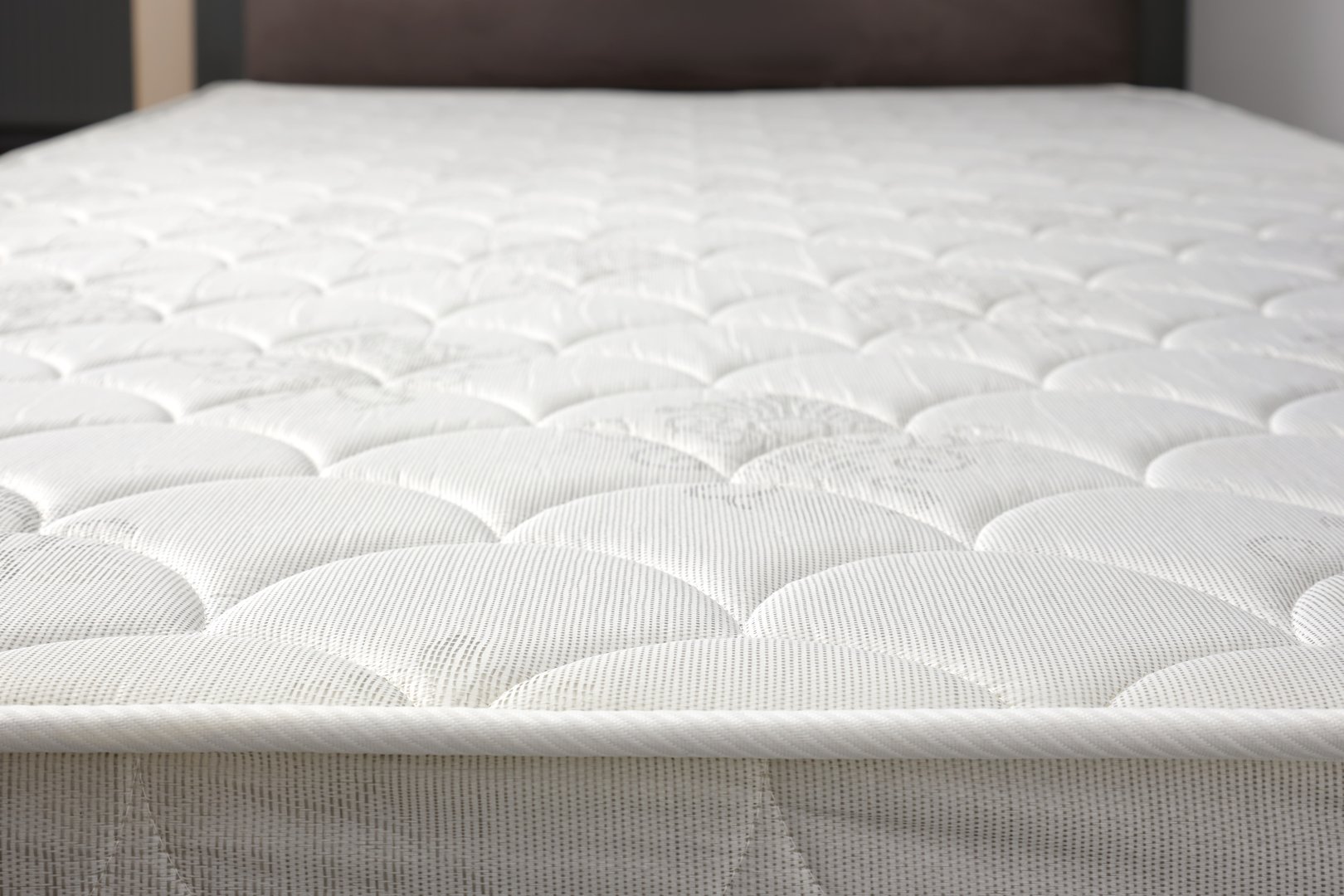 Close-up a new white mattress on grey bed in small apartment or house. Bed edge. Selective focus.