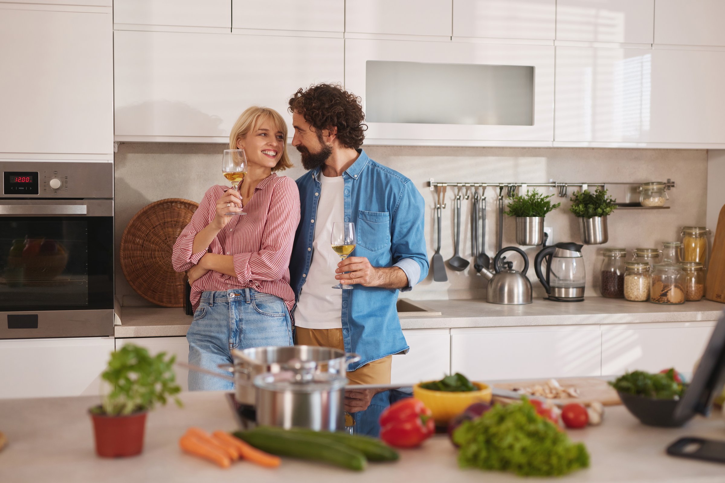 Smiling young couple having wine glasses in their modern kitchen preparing a healthy meal