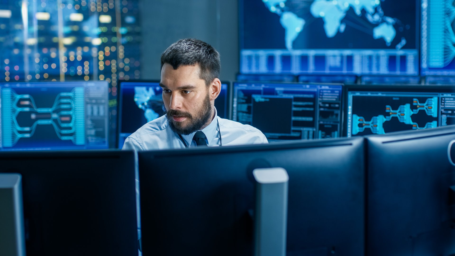 In the System Control Center Operator Working Surrounded by Displays Showing Relevant Data. In the Background Data with Interactive Map.