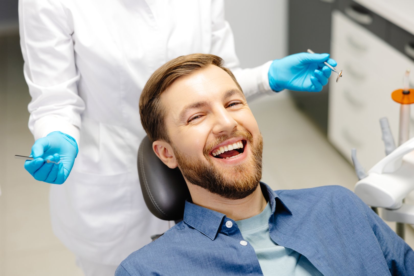 Portrait of happy man sitting at dentist chair in modern clinic and smiling. Patient enjoying dental treatment with professional dentist.