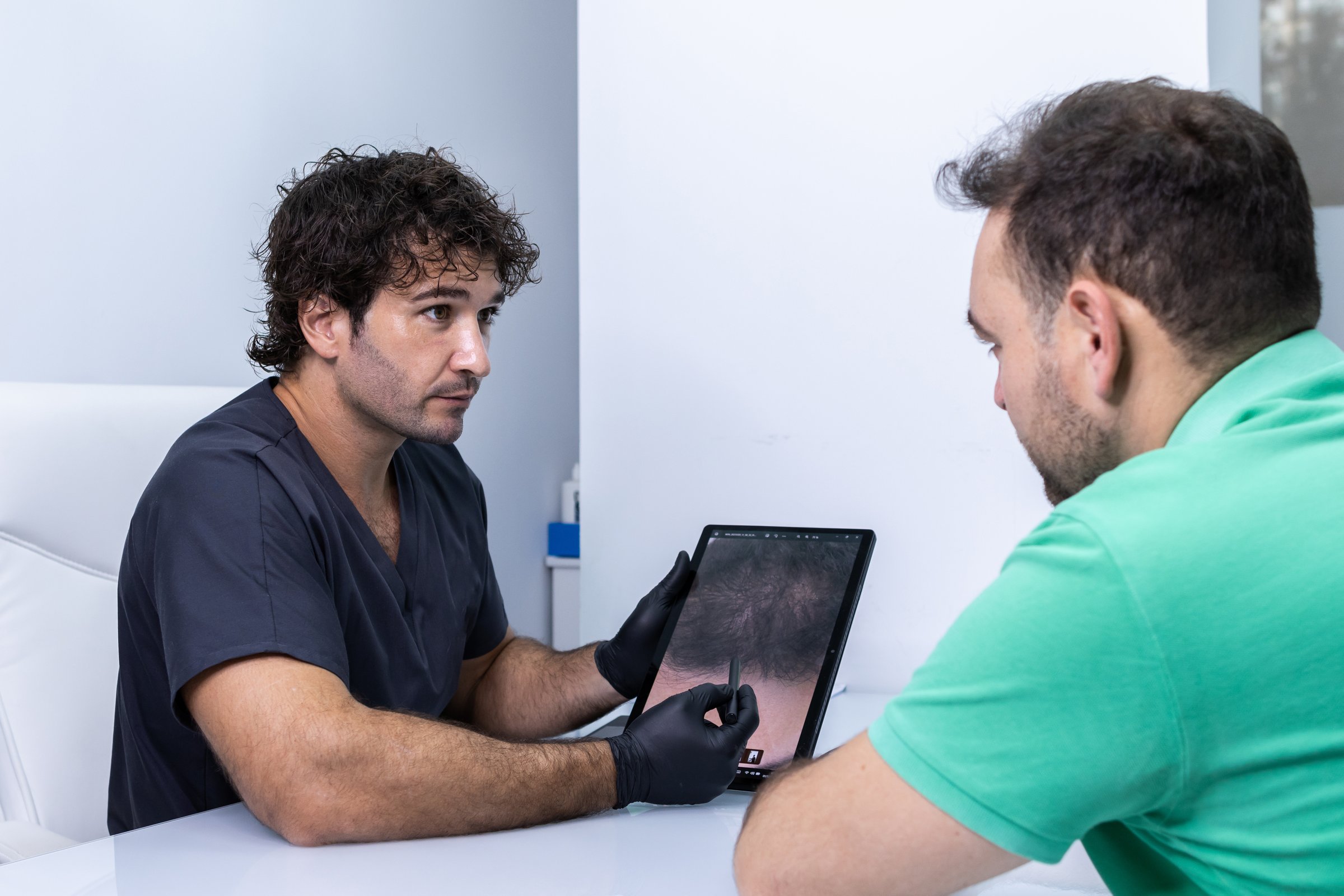Doctor explaining to his client with the digital tablet what is the procedure for hair treatment before the operation.