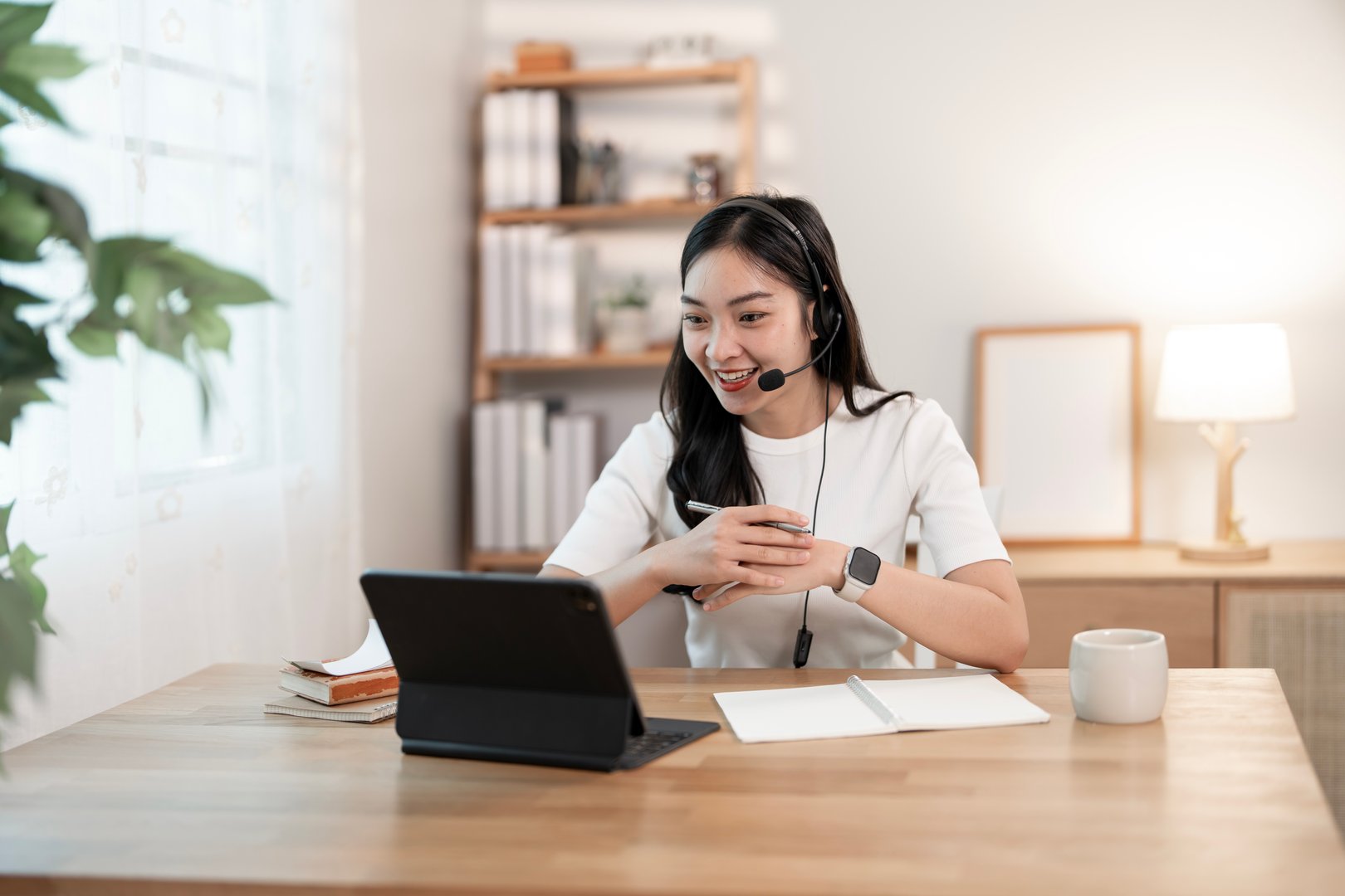 Happy Asian business woman with headset work from home with laptop, meeting online and video conferencing.