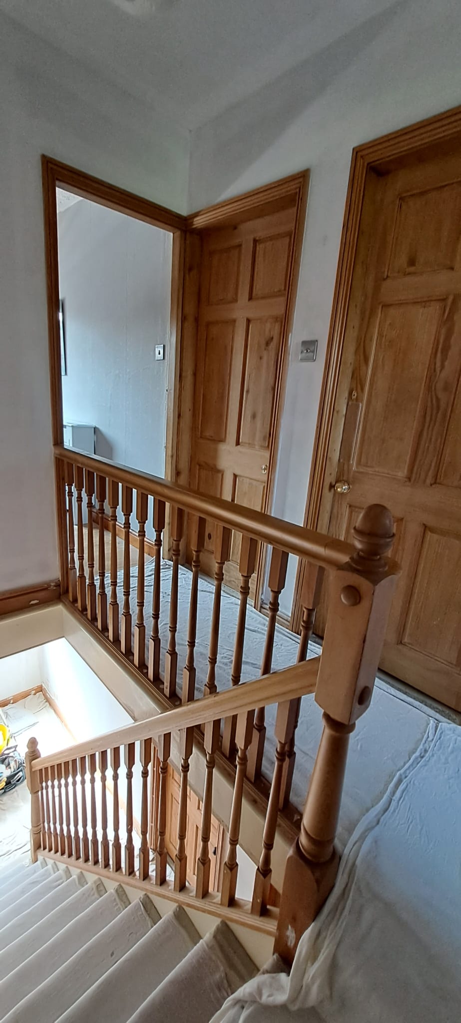 Wooden staircase with railing leading to a landing with two wooden doors and white walls.