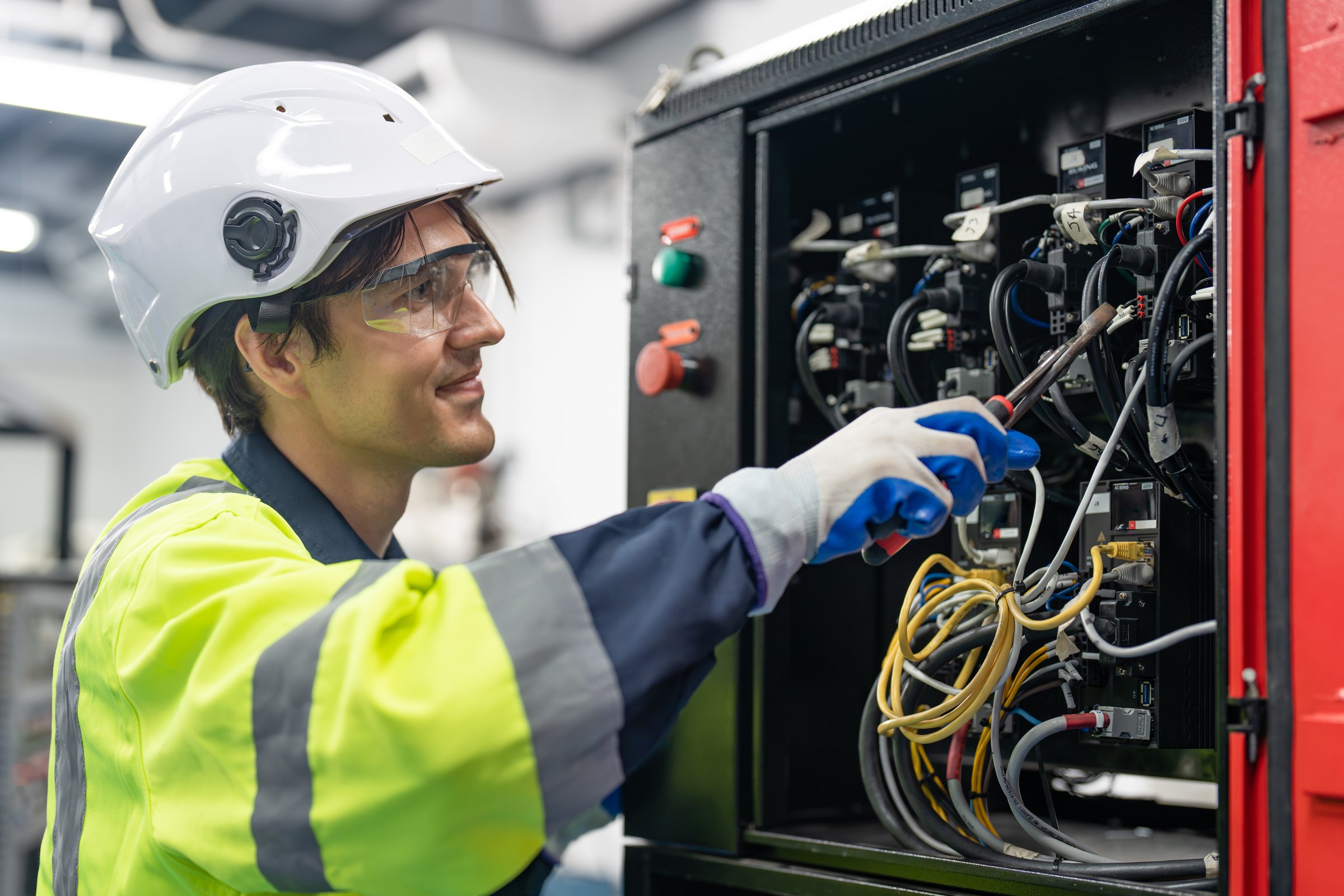 Happy engineer electrical man wearing helmet safety protection installing wire cable and breaker switch electric control in cabinet.
