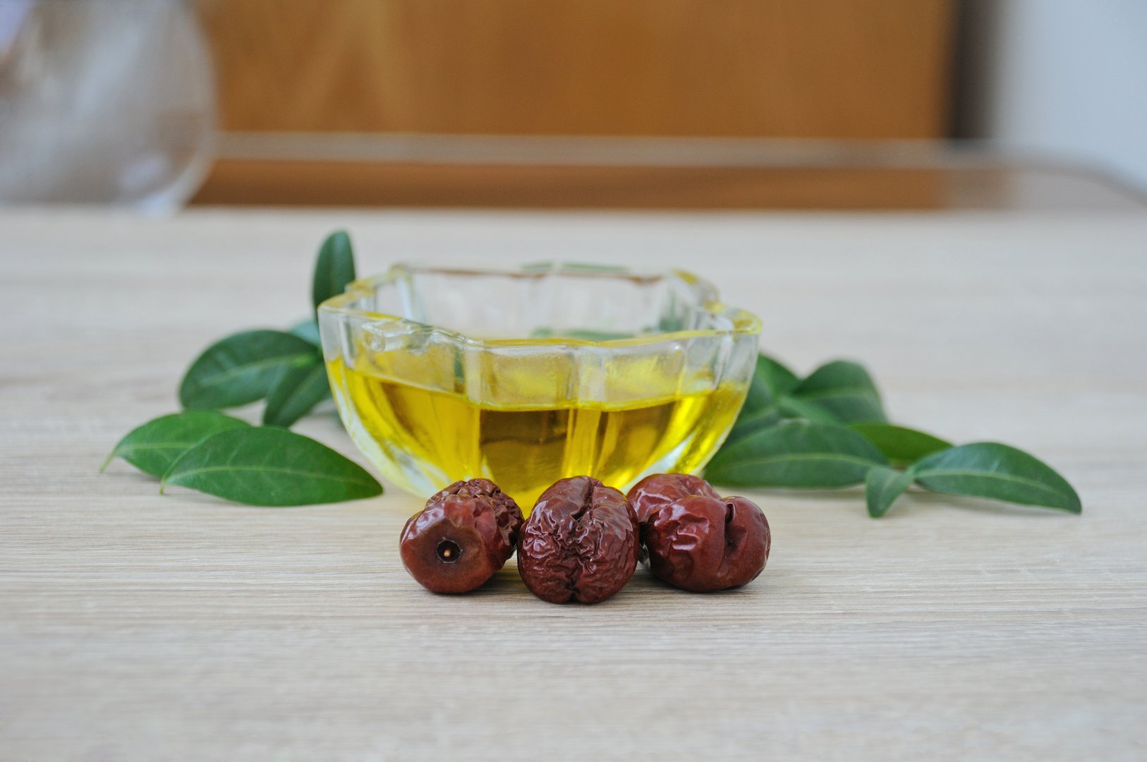 Jojoba fruits on the background of a cup with oil and green leaves. Selective focus on the anterior surface of the fruit.