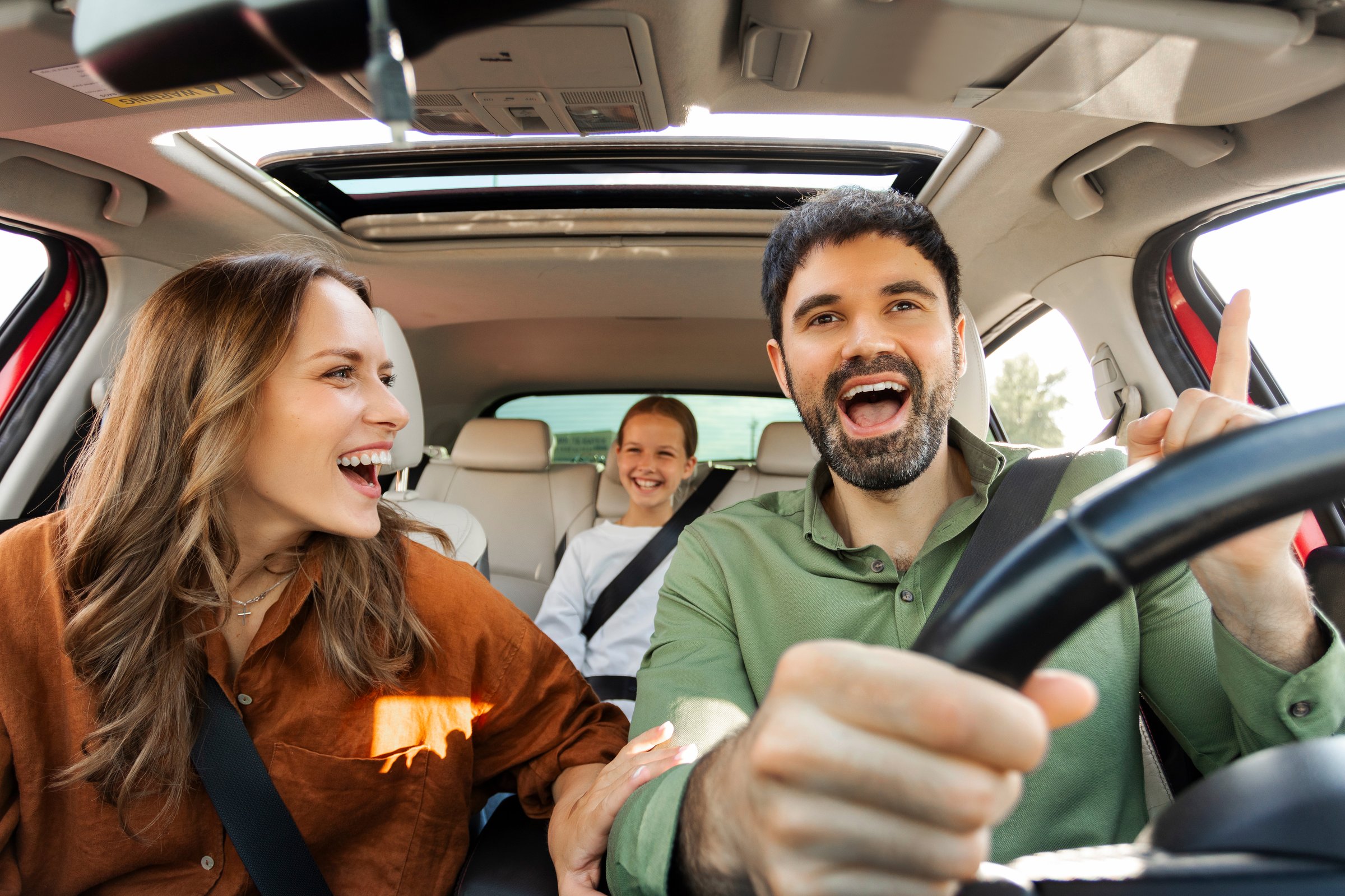 Excited European family of three driving car, enjoying music, singing and smiling, parents and child going on vacation, windshield view