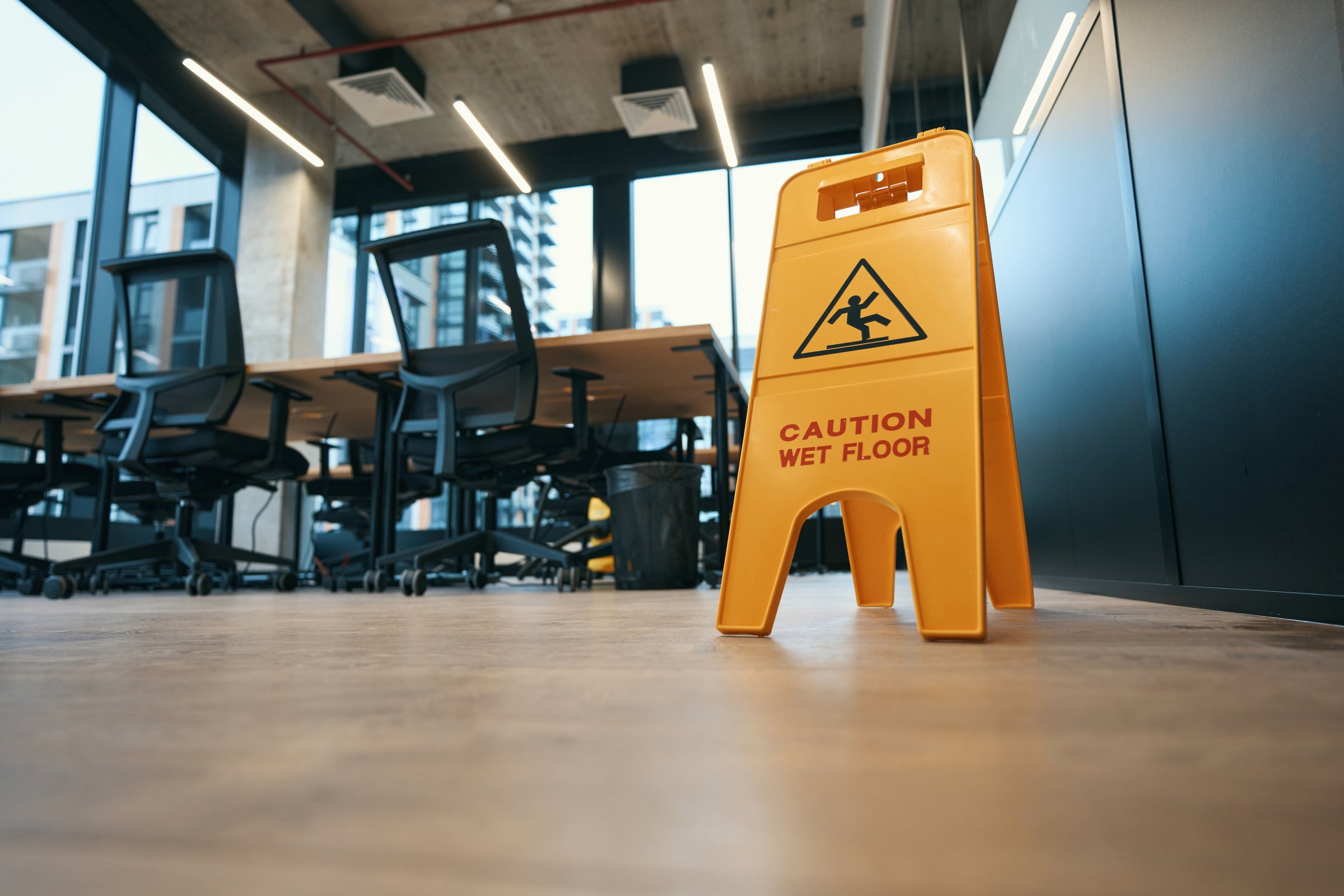 Warning sign Caution wet floor stands in the coworking area on the floor, chairs, tables and large windows in background
