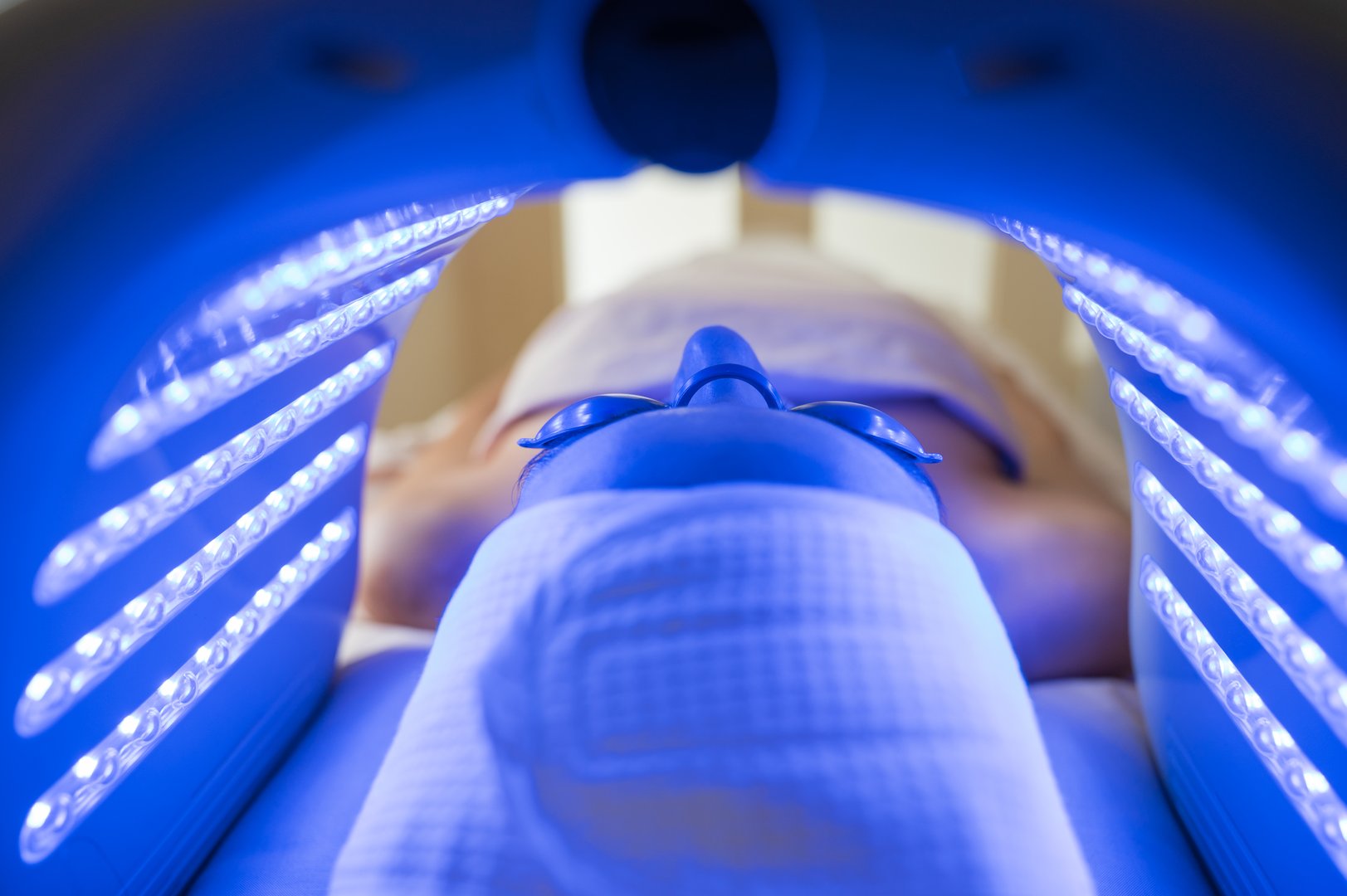 Young woman lying down with eye protection and receiving a Hydradermabrasian procedure with blue LED light therapy in a beauty center