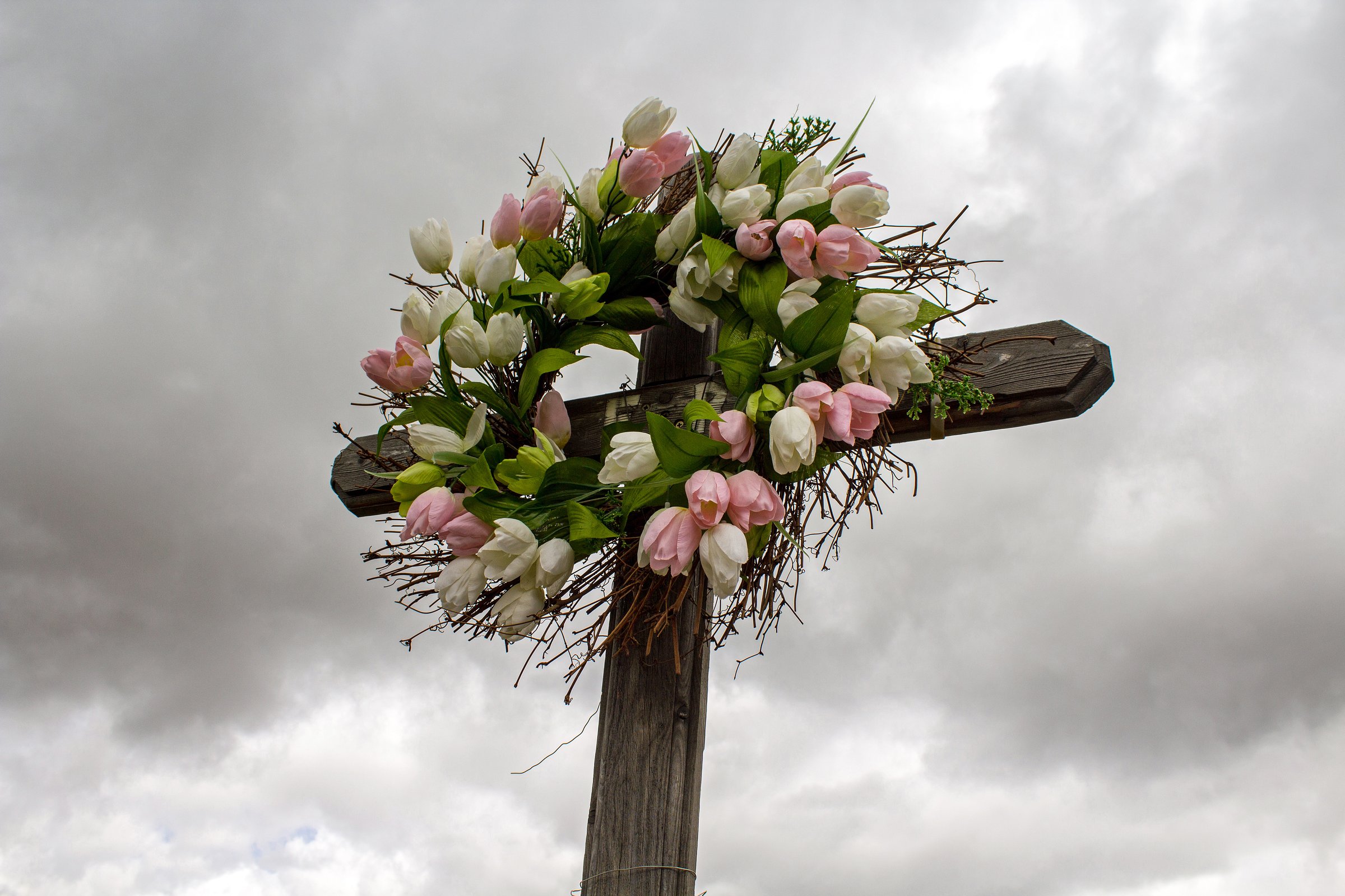 Simple Wooden Roadside Cross with a Wreath of White and Pink Silk Tulips