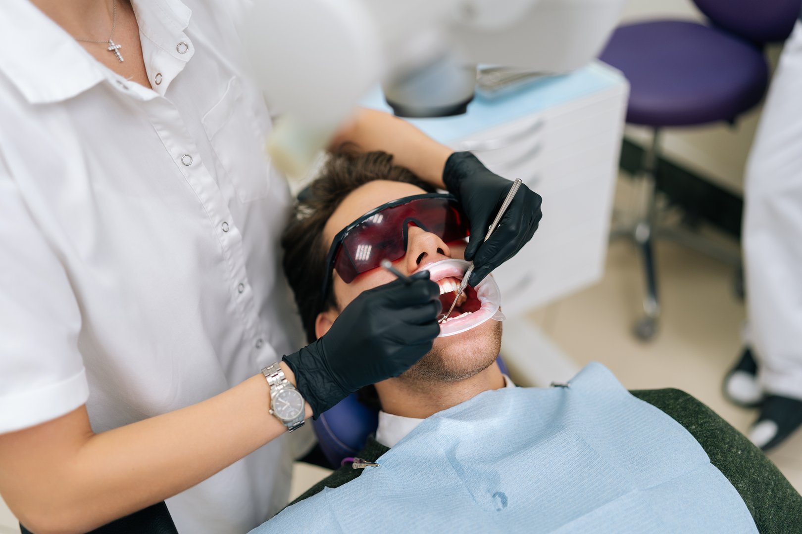 Closeup of unrecognizable female dentist using modern diode dental laser for periodontal care. Male patient wearing protective glasses, preventing eyesight damage. Periodontitis, dental hygiene.