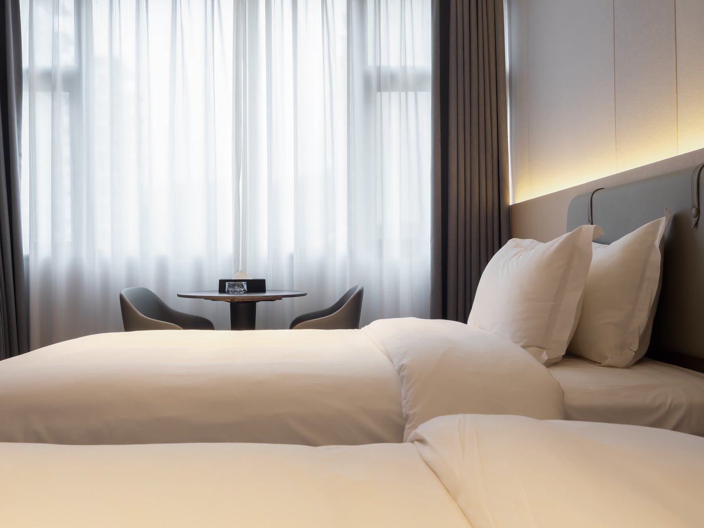 Clean hotel bedroom background with neatly arranged white bedding, soft lighting, and peaceful atmosphere, ideal for concepts of relaxation, comfort, hospitality, and premium travel accommodation.