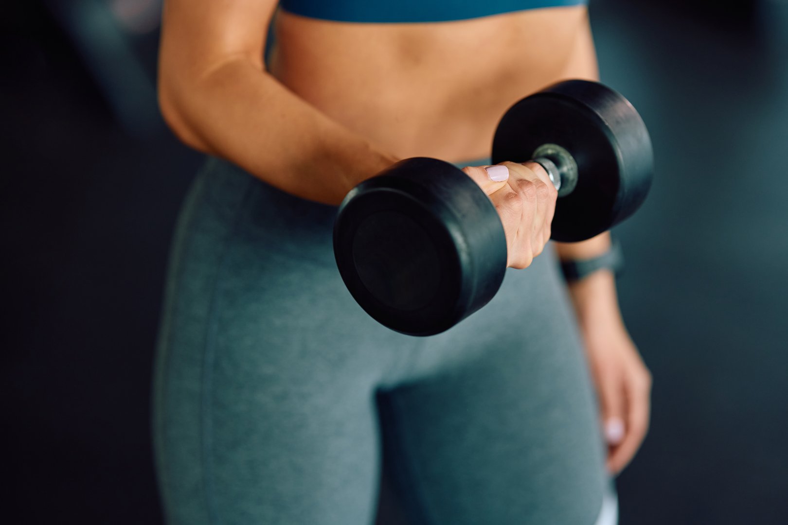Close up of athletic woman exercising with dumbbells in a gym.