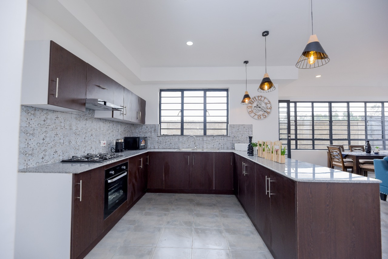 Modern kitchen with dark wood cabinets, patterned backsplash, and pendant lights over a granite countertop.