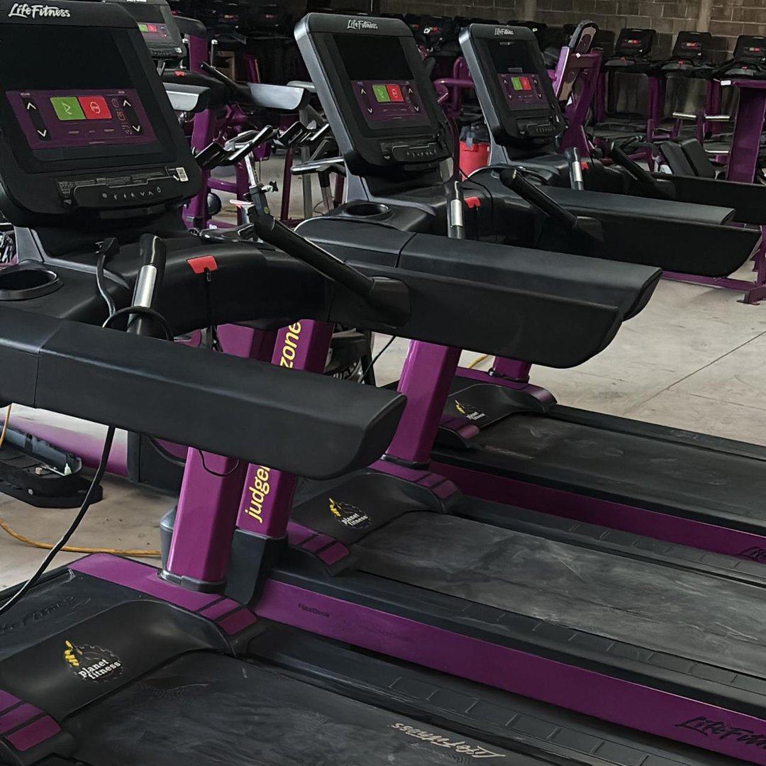 Row of purple treadmills with digital screens in an empty gym.