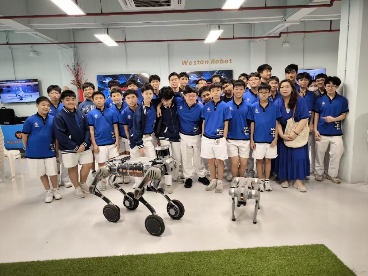 A group of students in blue shirts poses with two robot dogs in a room labeled Weston Robot.