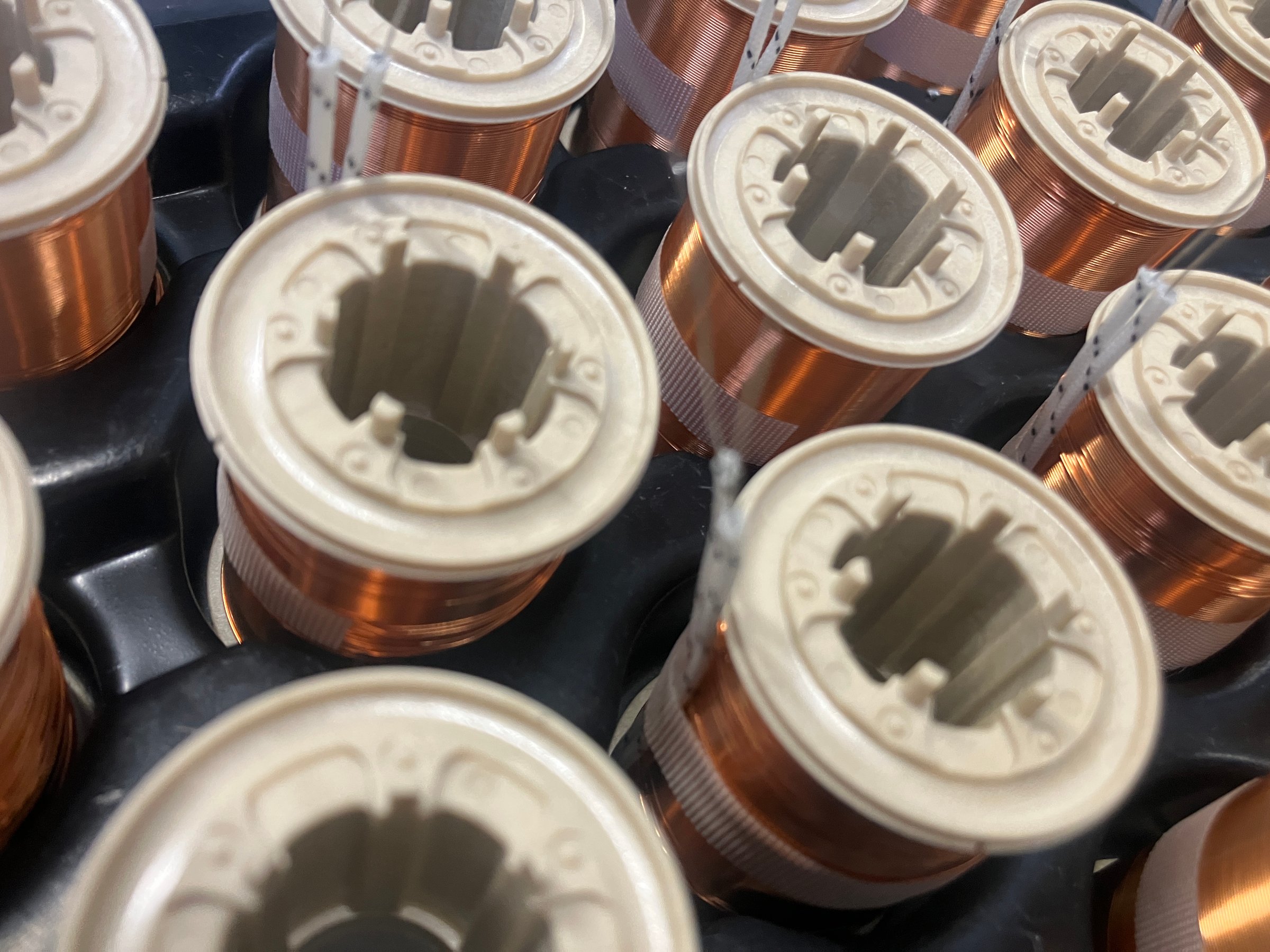 Close-up of industrial copper wire coils, meticulously wound around cylindrical cores. The image showcases precision engineering, electrical conductivity, and manufacturing aesthetics in modern technology and power applications. High quality photo