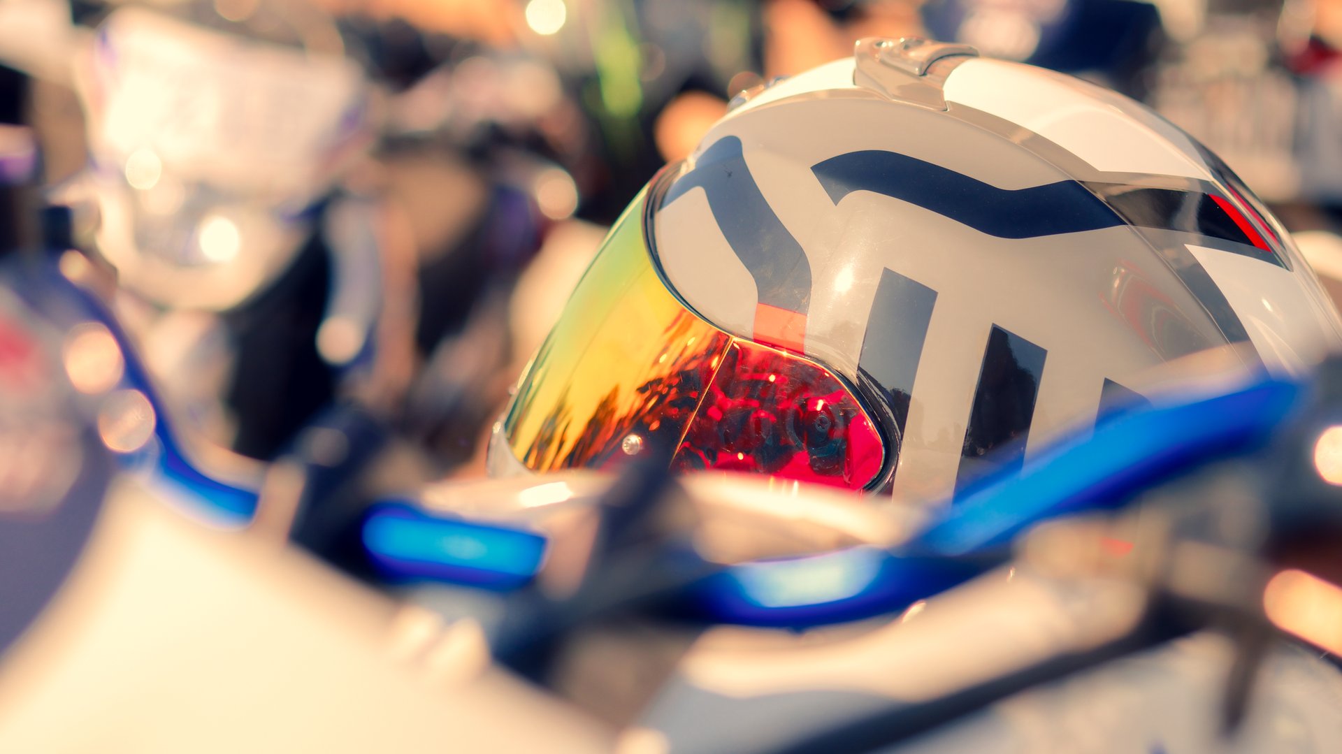 A motorcycle helmet with a blue stripe and a red stripe. The motorcycle is parked