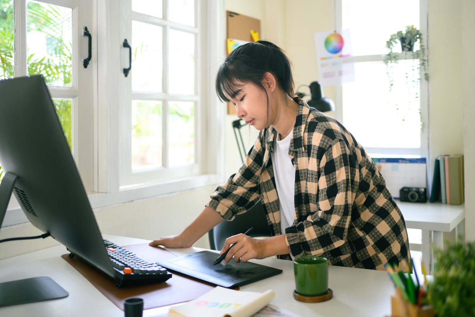 Creative designer working with computer and using stylus pen in bright modern office workspace.