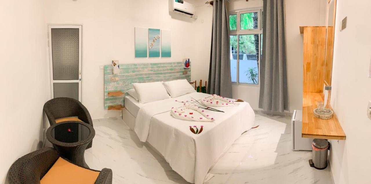 Bright hotel room with a double bed, decorated towels, two wicker chairs, a wall-mounted TV, and a large window.
