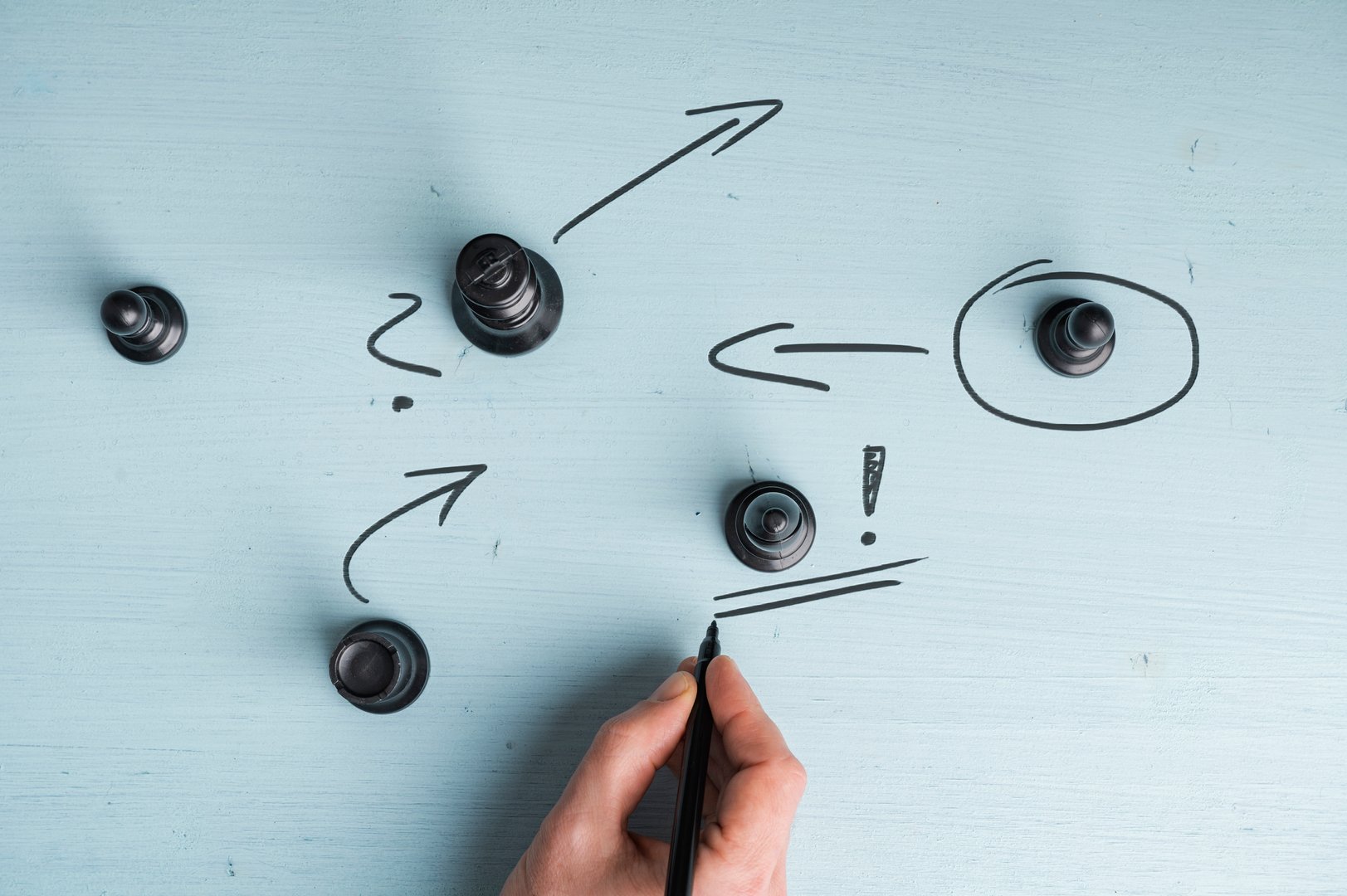 A hand draws arrows and symbols around chess pieces on a blue surface, illustrating strategy and planning of a business or startup company.