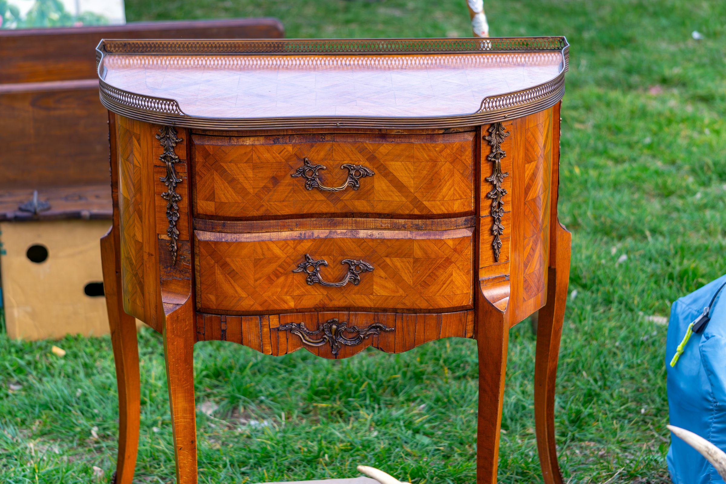 Stylish, antique chest of drawers with marble top. Wooden chest of drawers with richly decorated fronts and metal handles for sale at a flea market