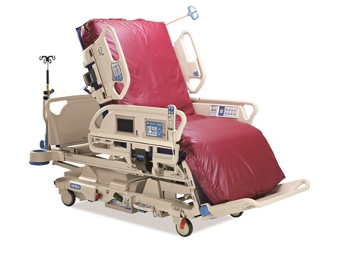 A hospital bed with red bedding, adjustable side rails, electronic controls, and an IV pole on wheels.