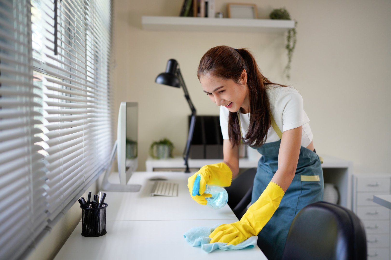 young woman in yellow gloves cleaning the table in the office.