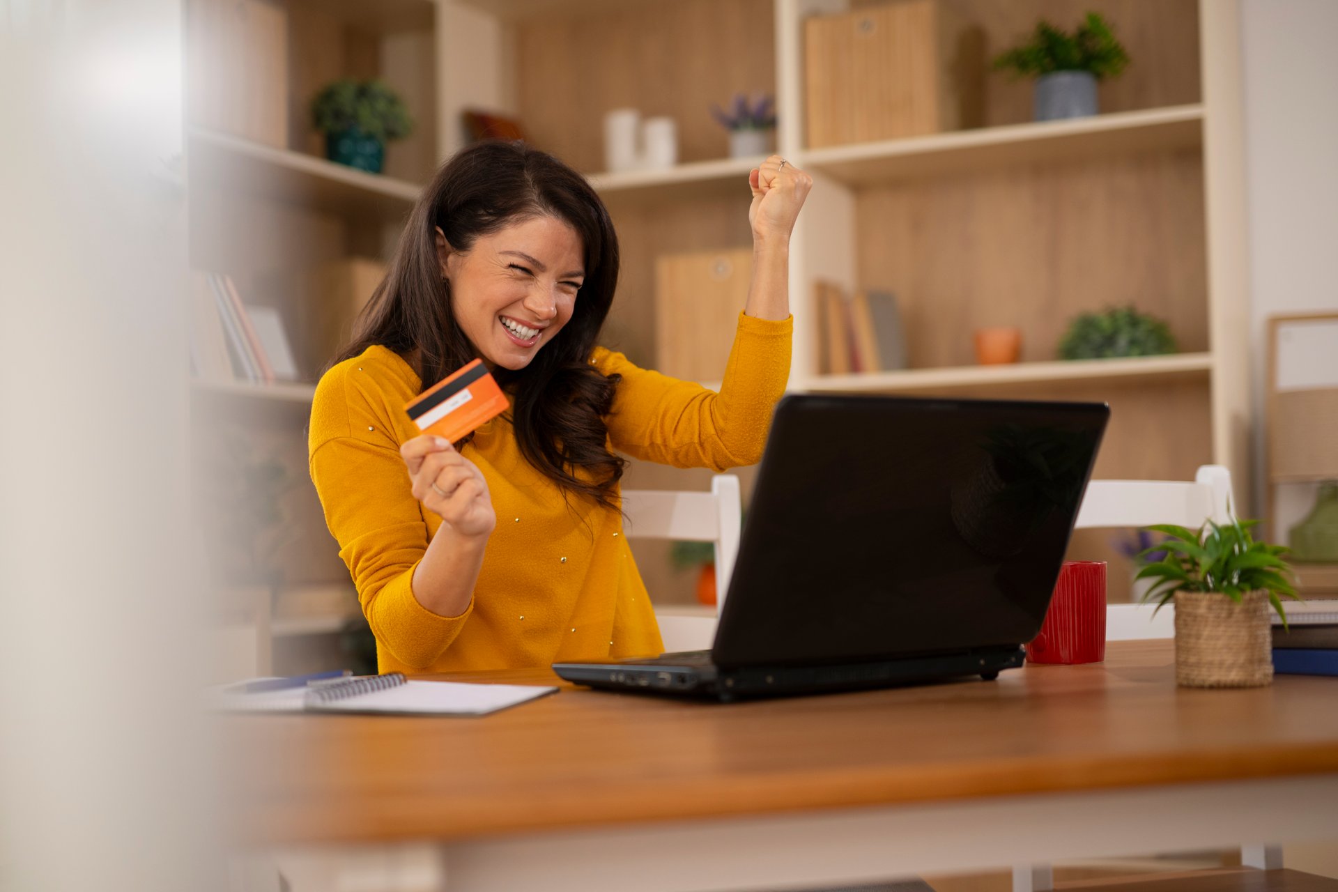 Woman feeling excited and celebrating success with a credit card during online shopping at home