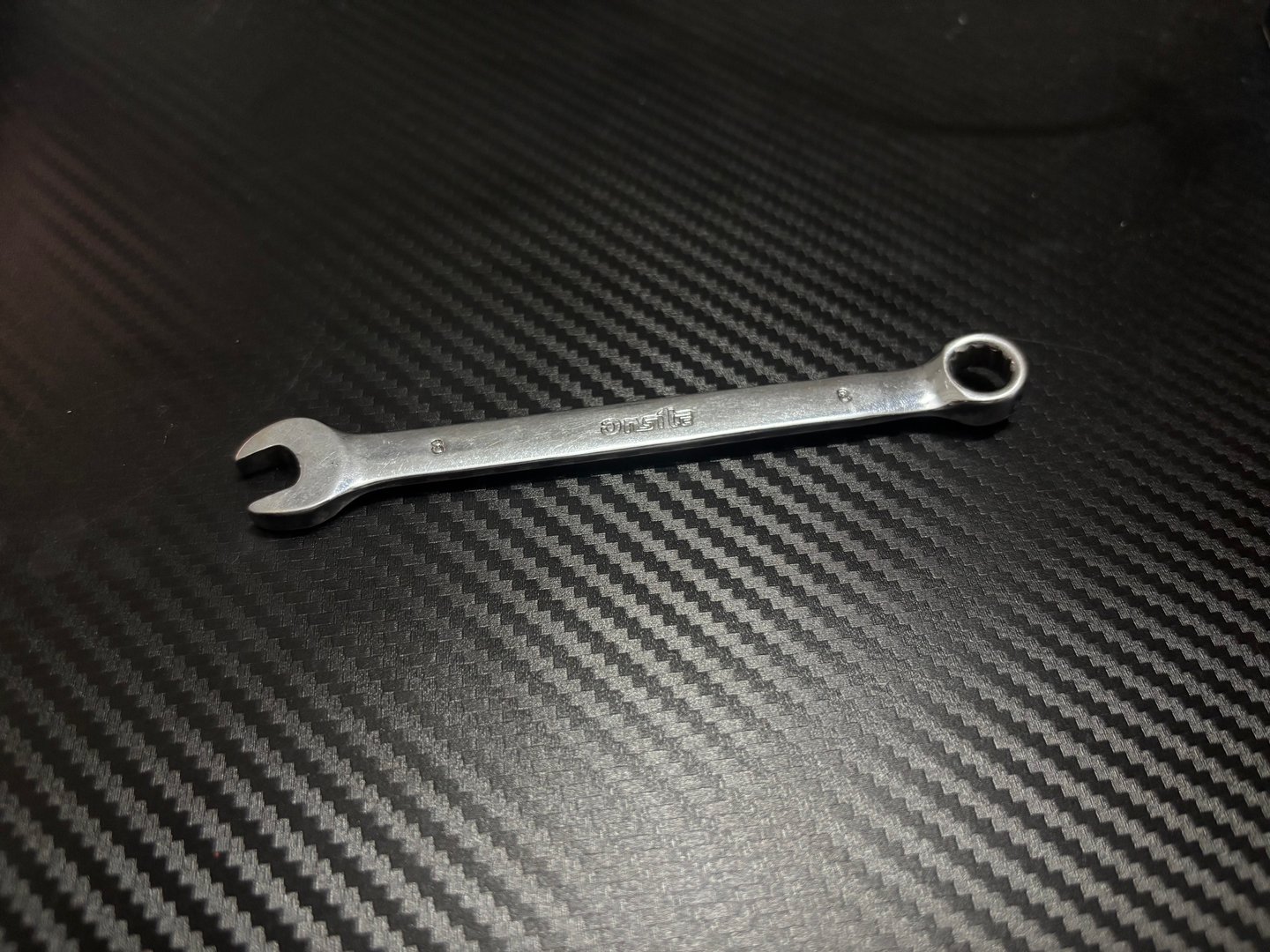 Metal combination wrench on carbon fiber texture background, minimal industrial tool concept
