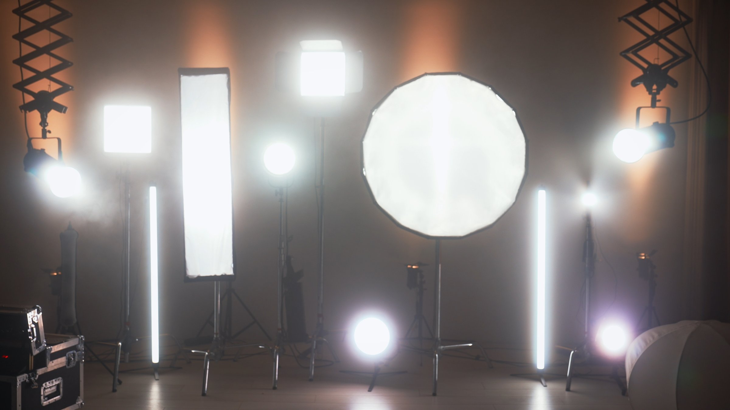 Multiple studio lights, softboxes, and LED panels illuminating a film set. Equipment includes vertical tubes, octaboxes, and overhead lighting mounts. Backstage preparation for studio professional shooting.