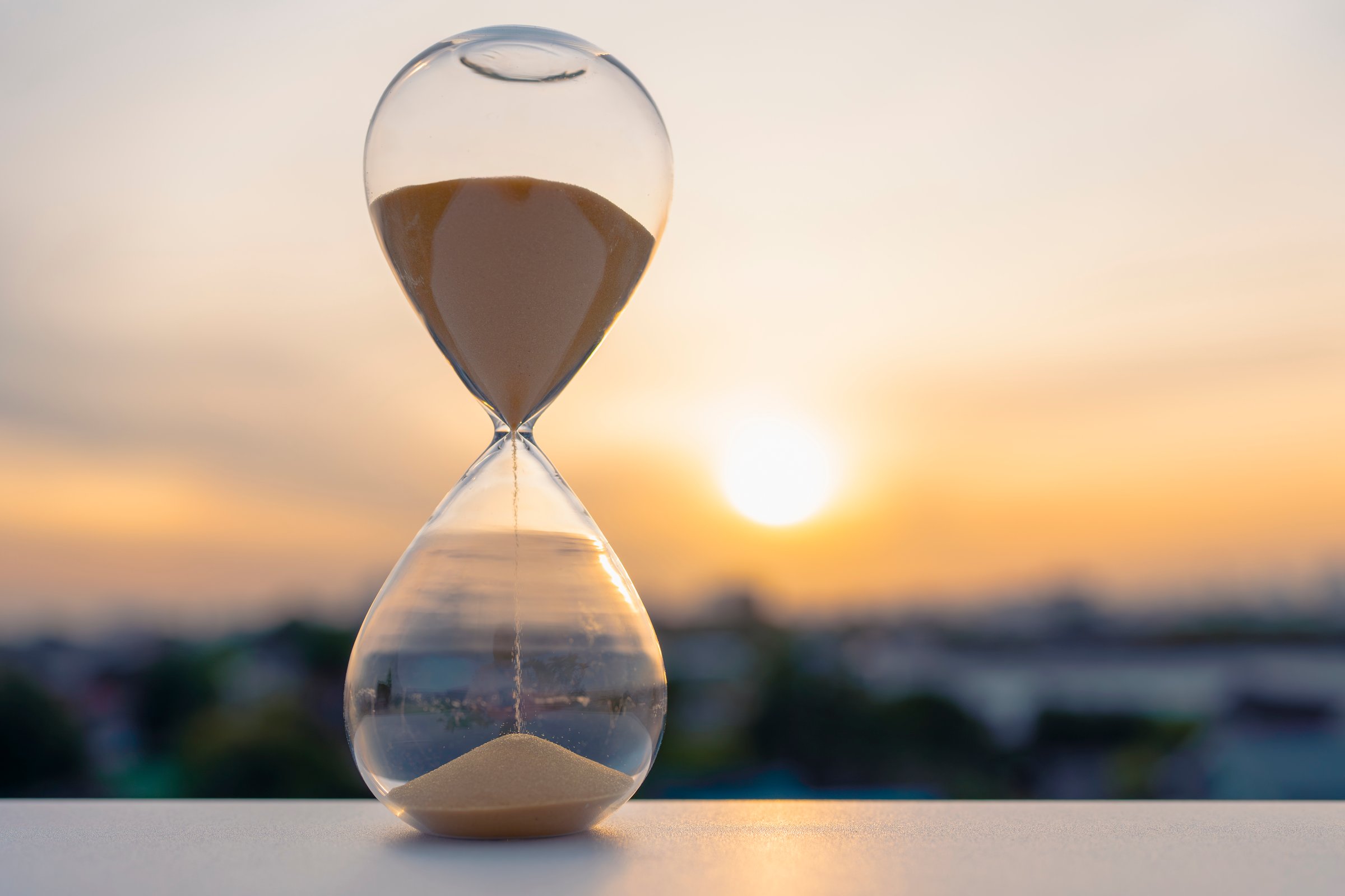 Hourglass with golden sand flowing at sunset symbolizing patience and time
