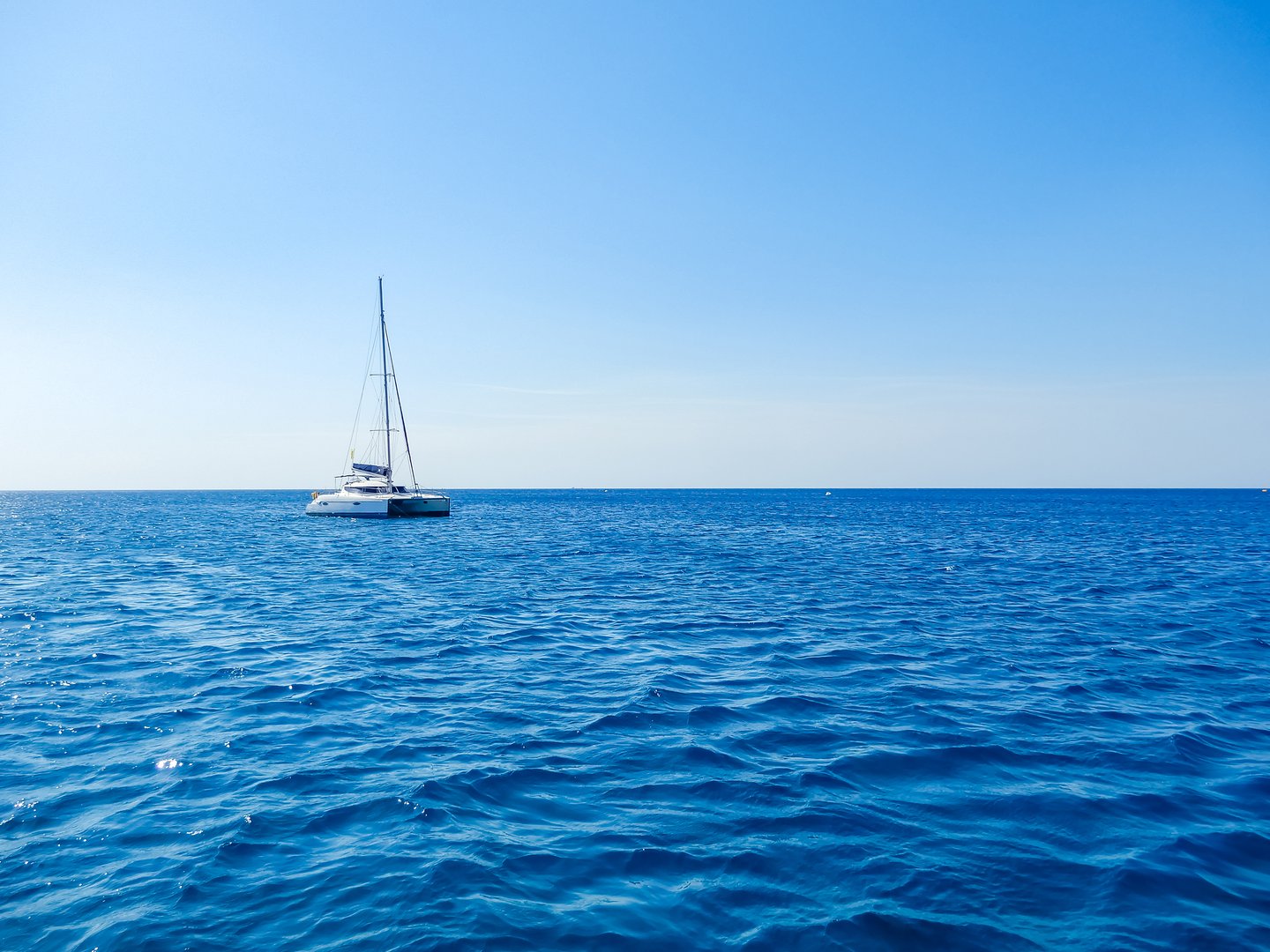 Sailboat drifting on calm blue ocean under clear sky, peaceful and serene scene. High quality photo