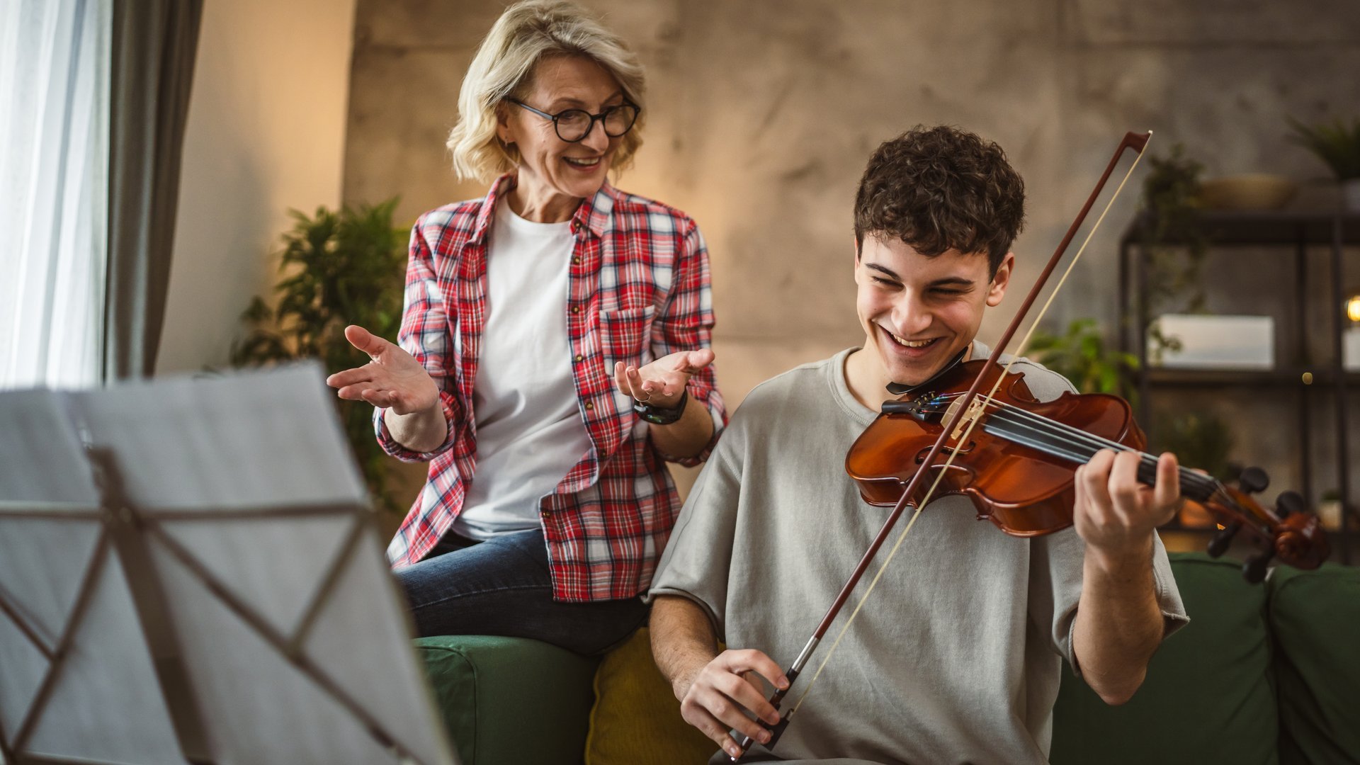 Young man learn how to play violin under instruction of mature woman female professor tutor at home take private class