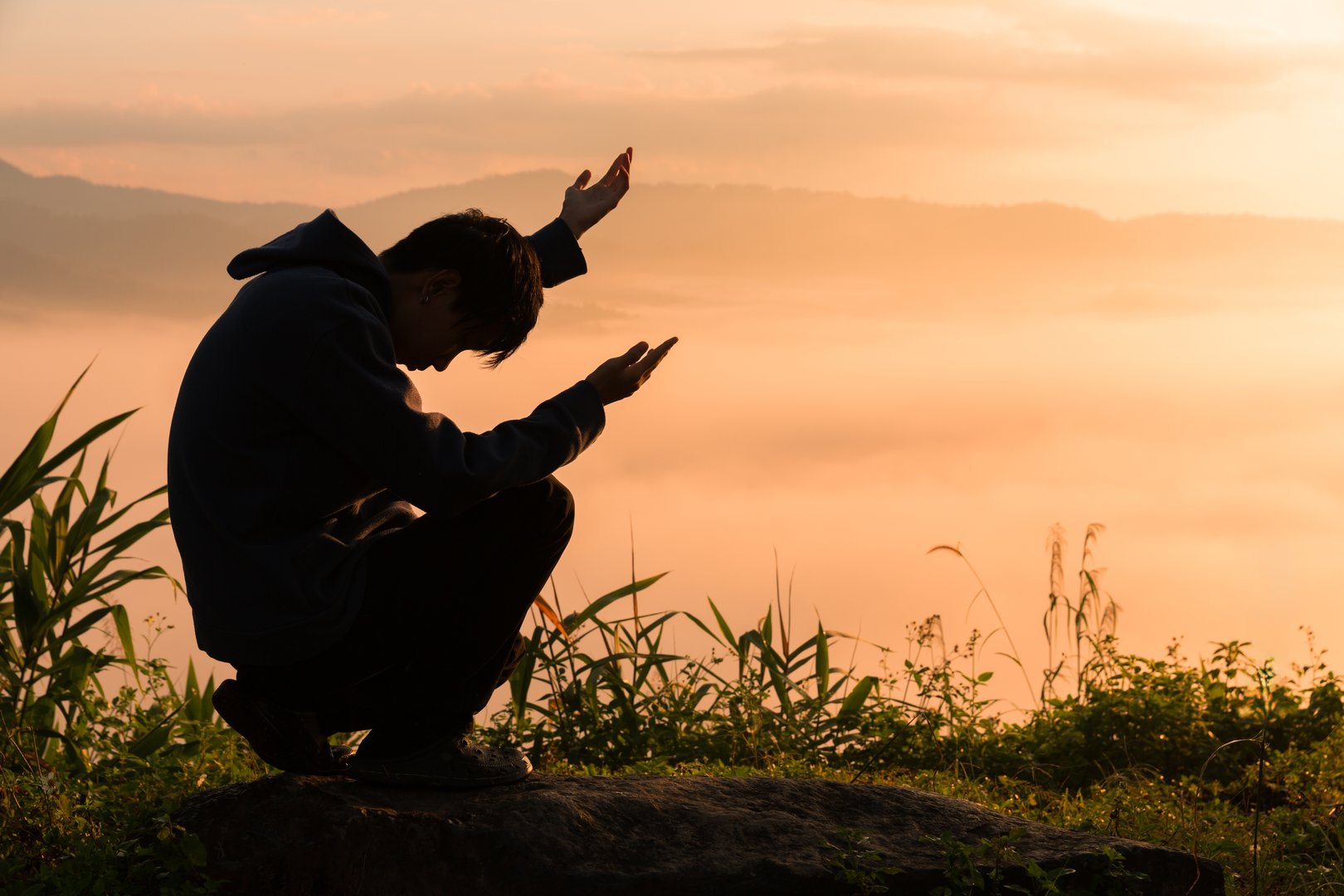 Christian man in silhouette, praying to God and worshiping Jesus Christ at sunset, seeking peace and reflection from sunrise to sunset.