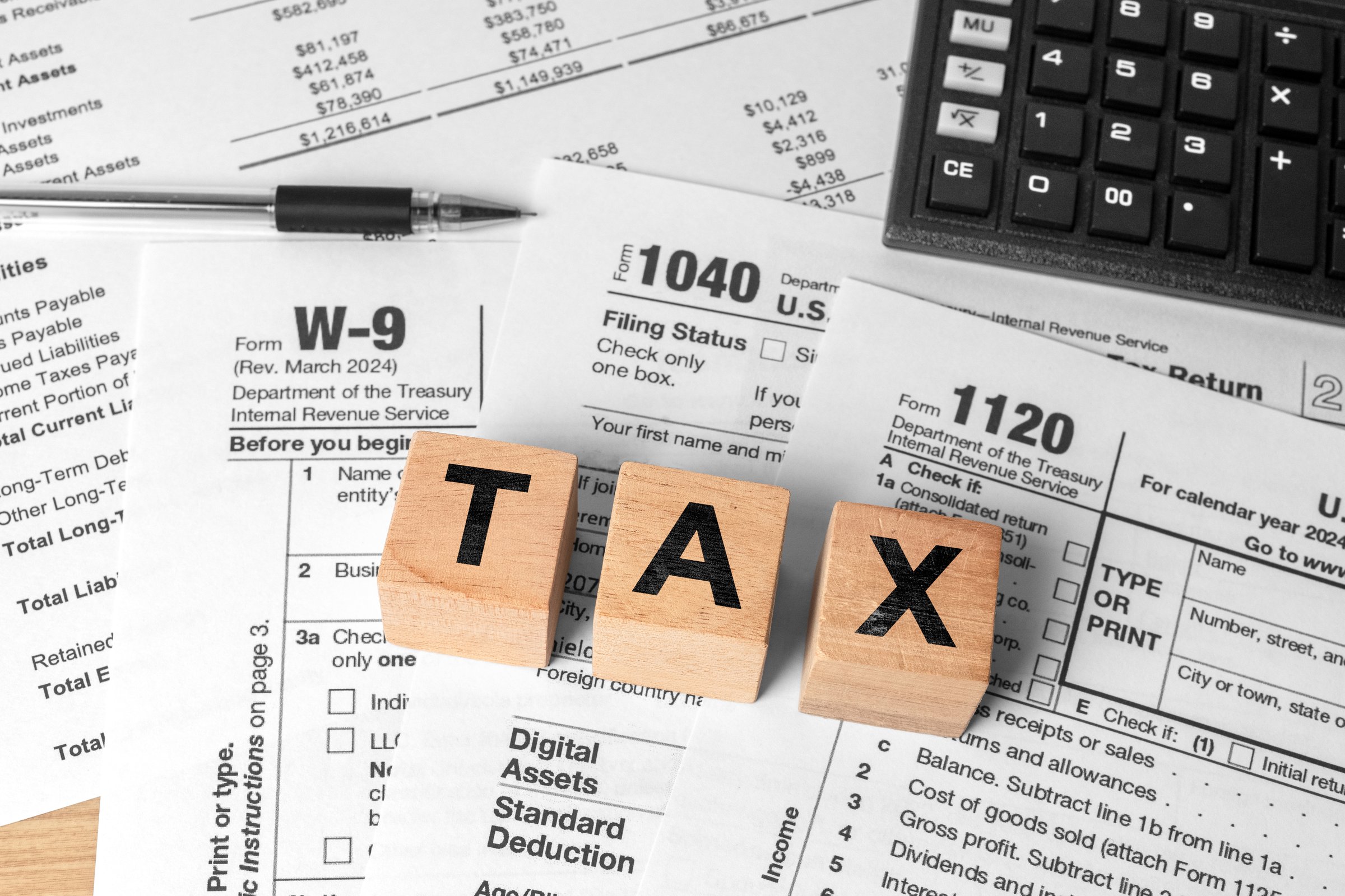 Tax season concept with wooden letter blocks, calculator, and pen on 1040 tax form. Income tax filing and financial planning background