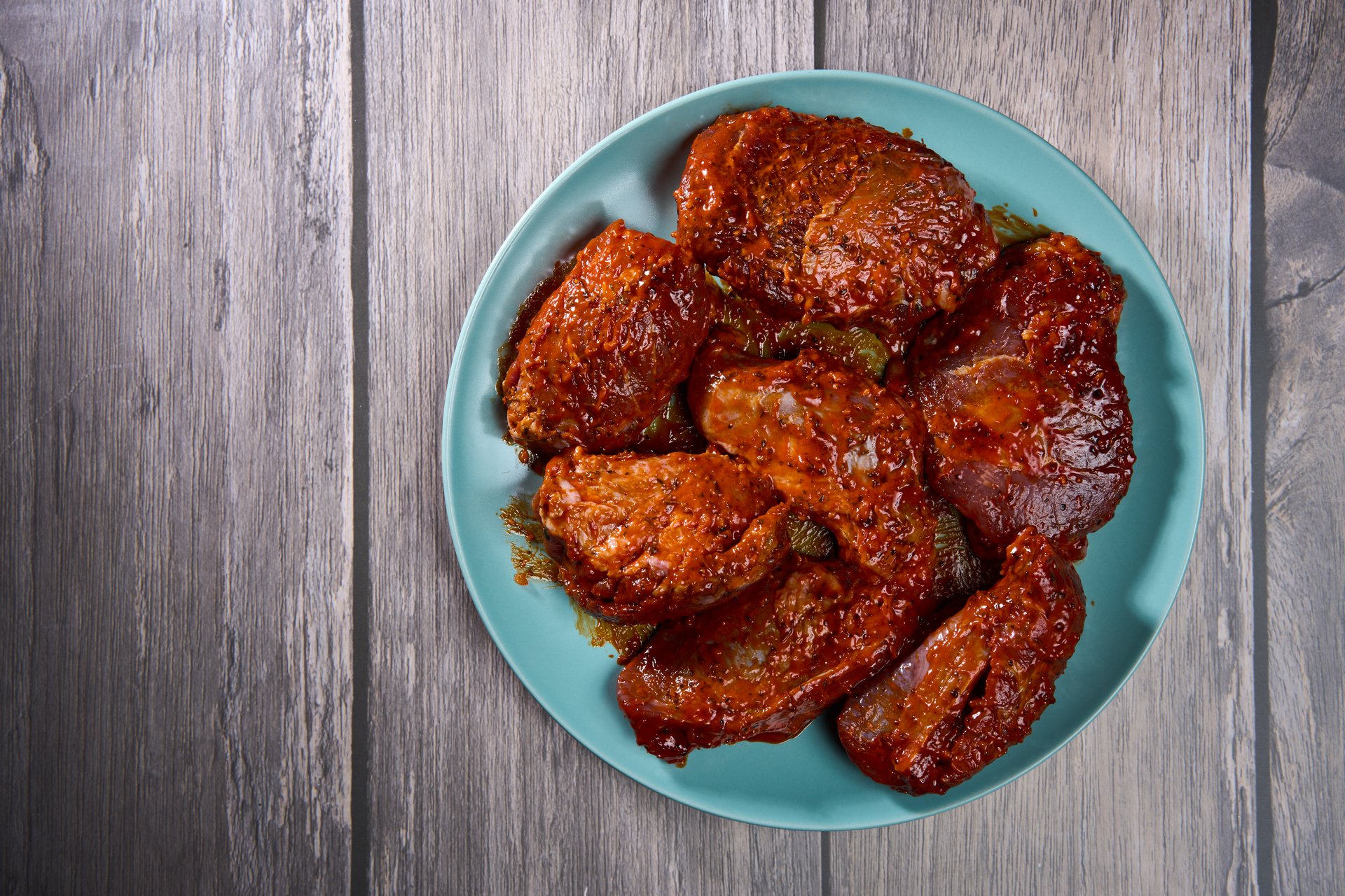 Marinated pork jowl (cheeks) fillets on a wooden board in closeup