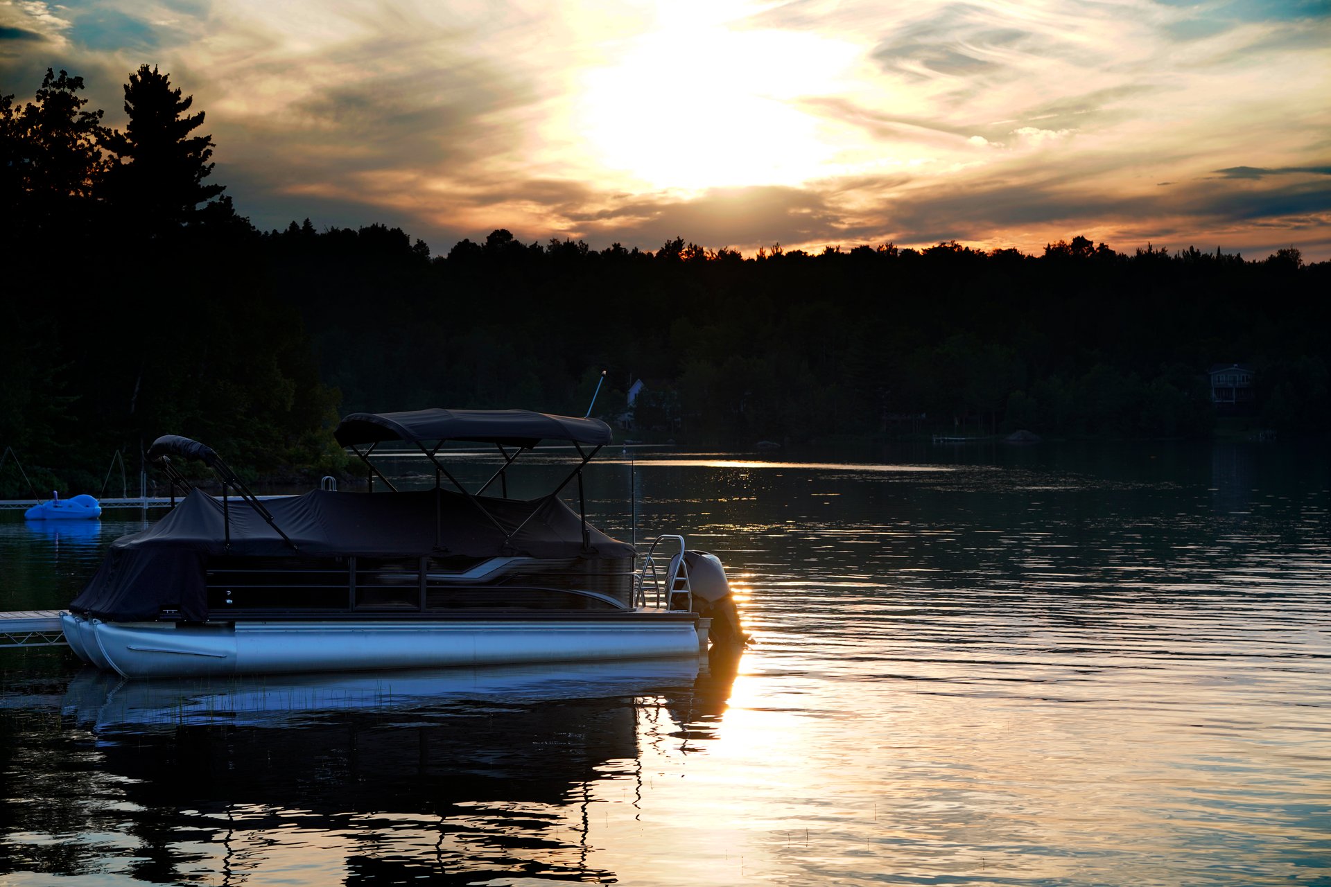 A picture of a pontoon boat on lake with a evening sunset