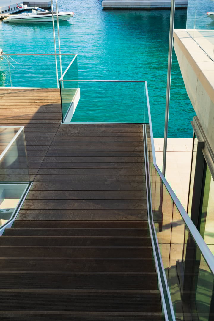 View down modern wooden stairs with glass railings to a luxury private pier in a marina with turquoise water.High quality photo