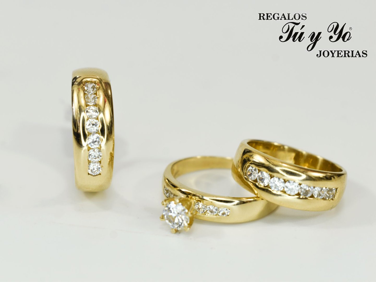 Three gold rings with diamond settings, including an engagement ring, displayed on a white surface with jewelry store logo.