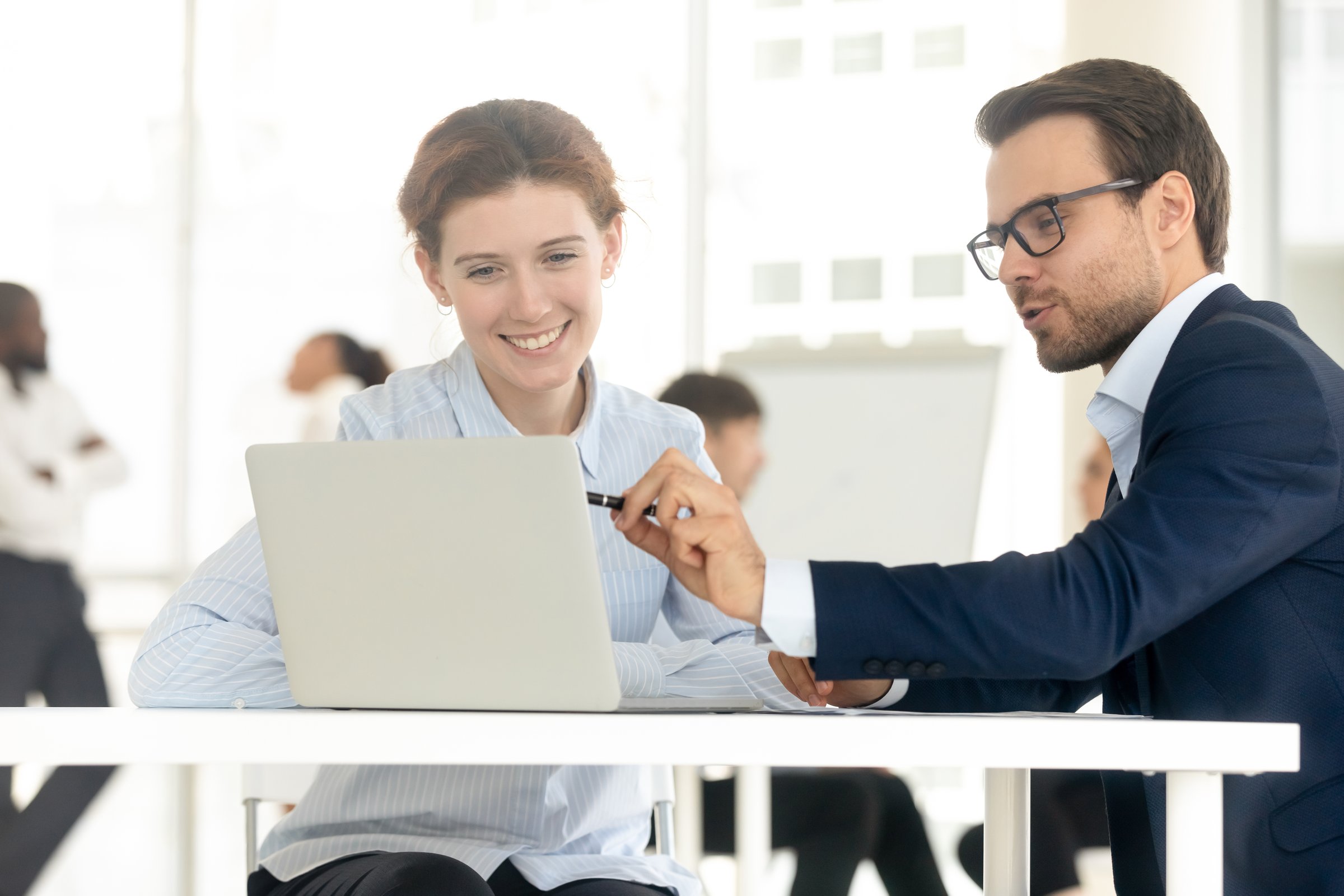 Smiling mentor coach businessman training businesswoman at personal meeting. Fun man employee consulting female client, male collegue point at laptop and presenting new project to female leader.