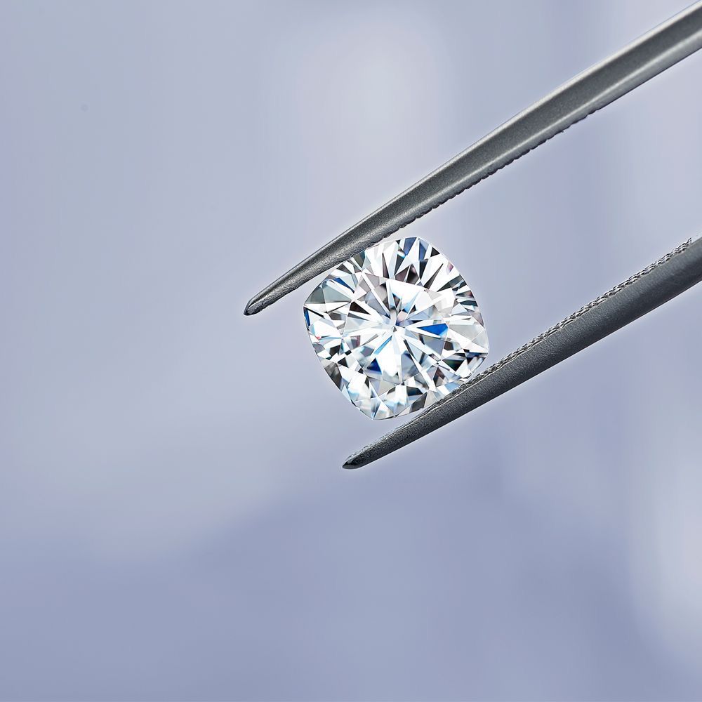 Close-up of a round diamond held by tweezers on a soft blue background.
